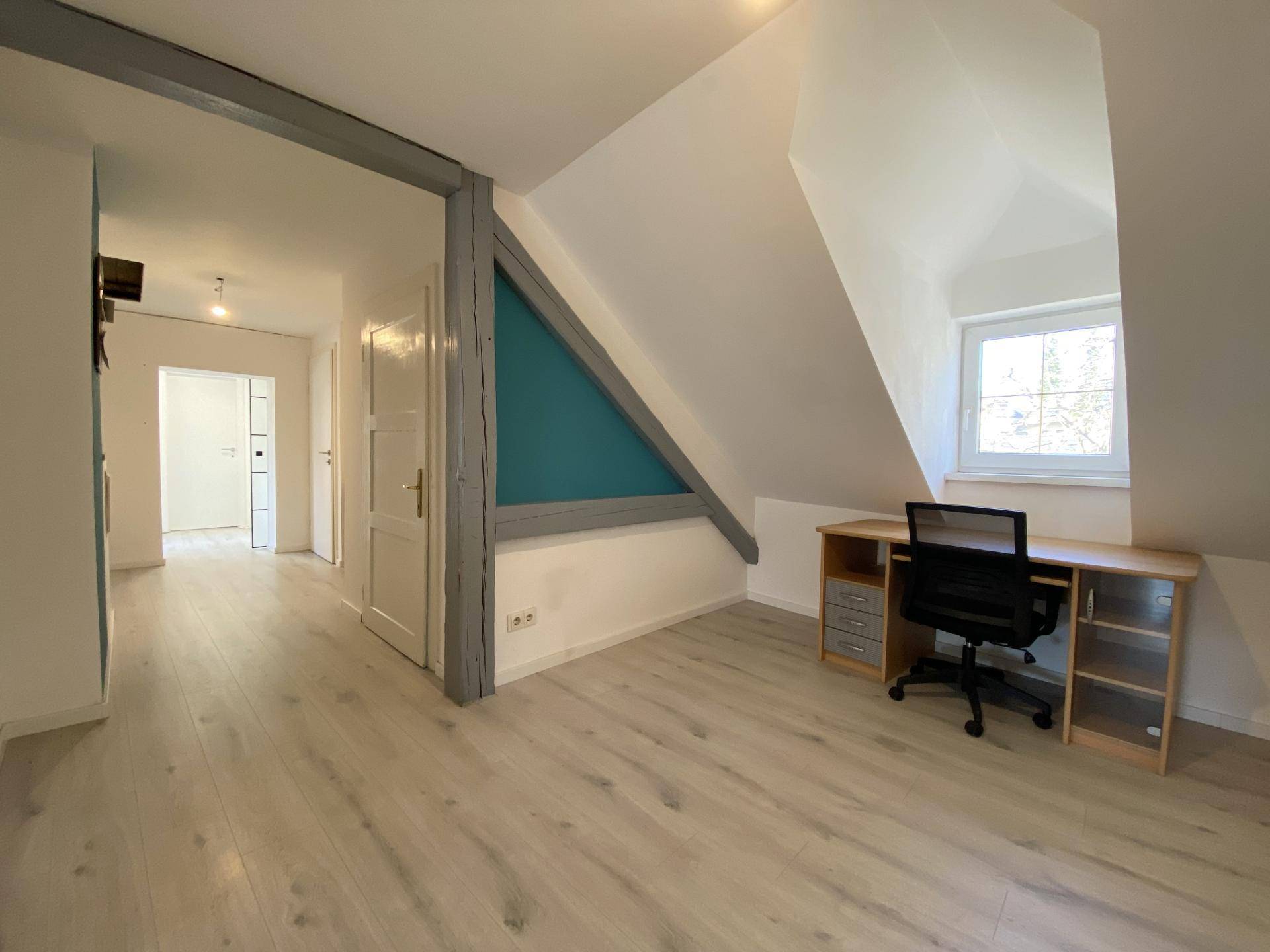 Helles Dachzimmer mit Laminatboden, Dachschräge und einem Fenster, das Tageslicht spendet.