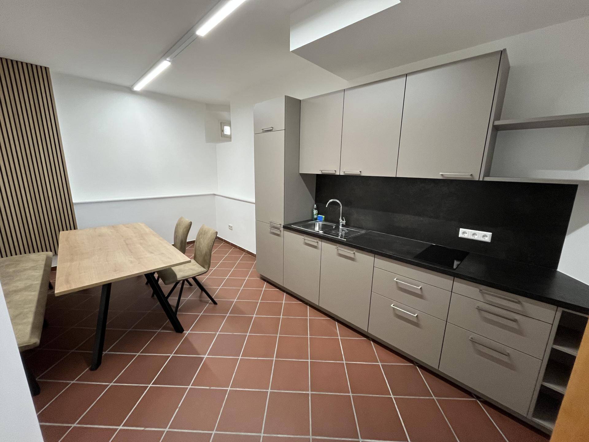 Moderne Küchenzeile mit hellgrauen Schränken, dunkler Arbeitsplatte und Essbereich mit Terrakottafliesen.