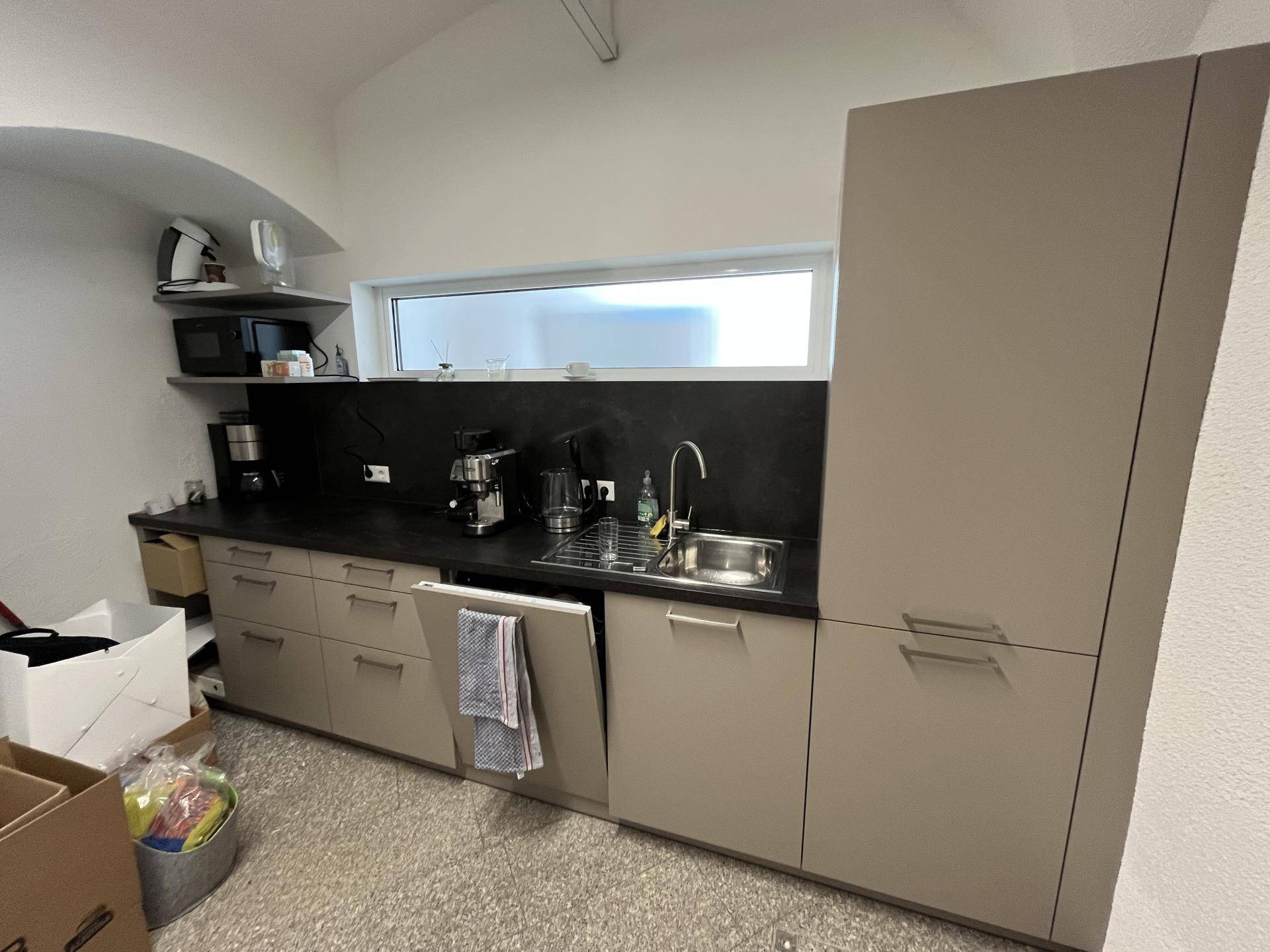 Moderne Küchenzeile mit hellgrauen Schränken, Spüle, Geschirrspüler und einem schmalen Fenster.