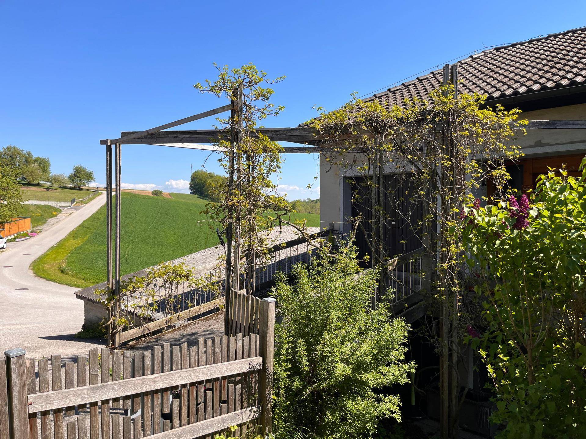 Überdachte Terrasse mit Holzpergola und weitem Blick über grüne Felder.