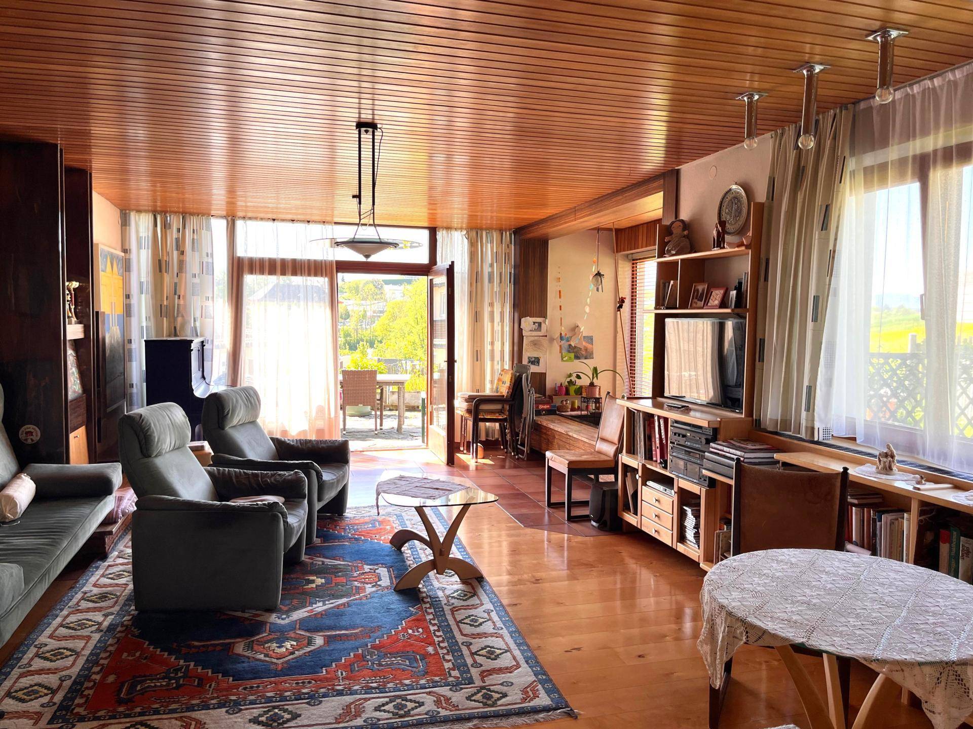 Geräumiges Wohnzimmer mit Holzboden, Holzdecke und Zugang zu einem Balkon.