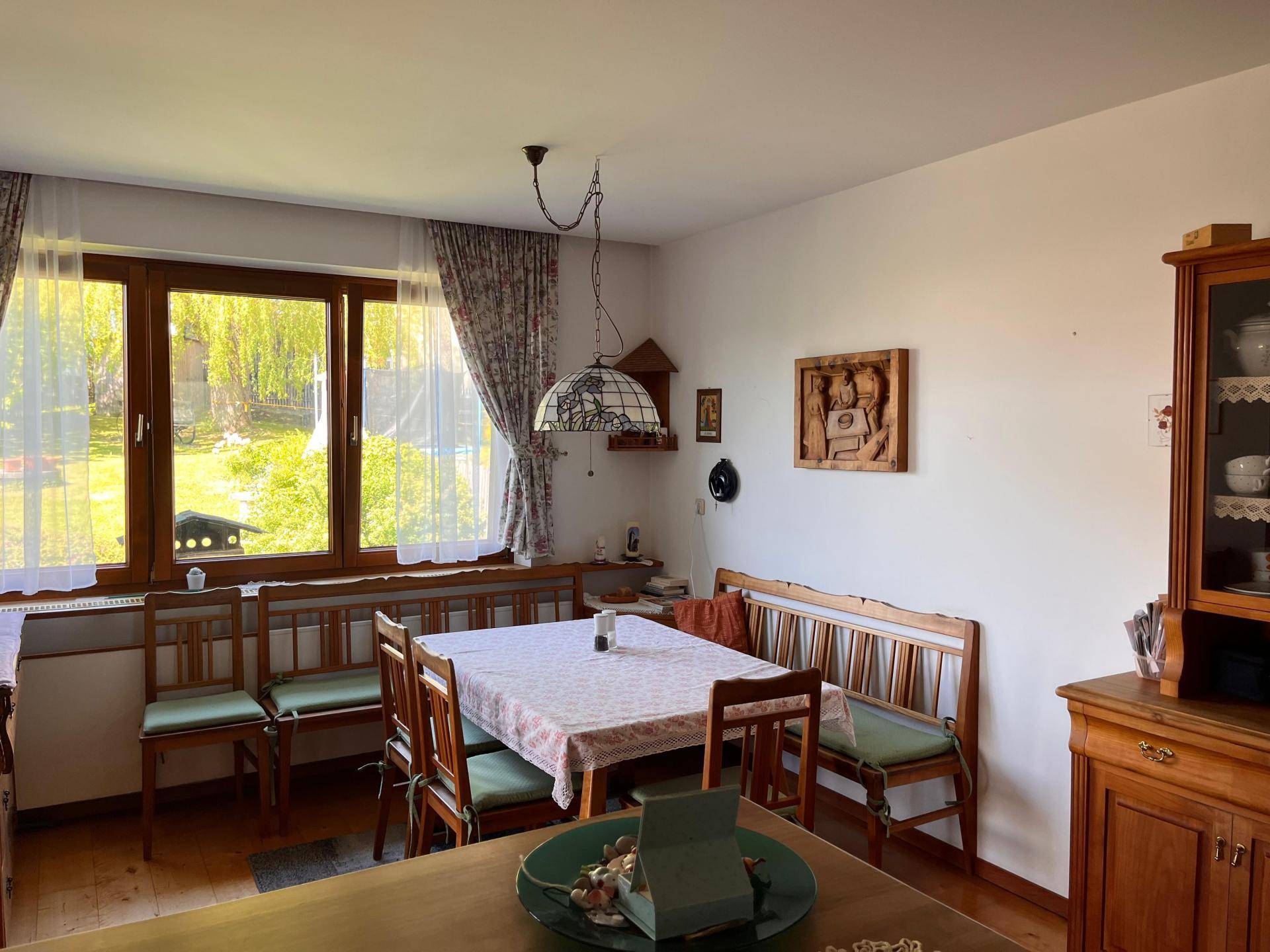 Traditioneller Essbereich mit Holztisch, Eckbank und Blick ins Grüne durch große Fenster.