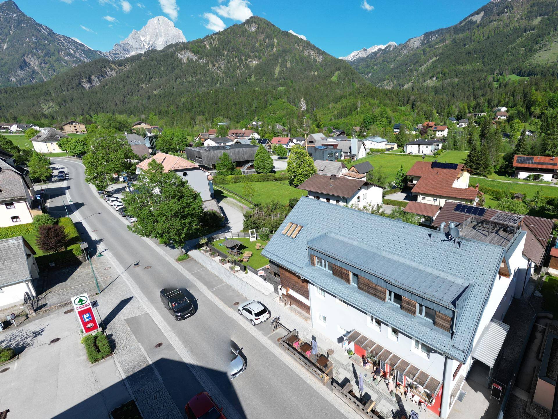 Luftaufnahme eines Gebäudes an einer Straße mit Bergkulisse und umliegenden Häusern.