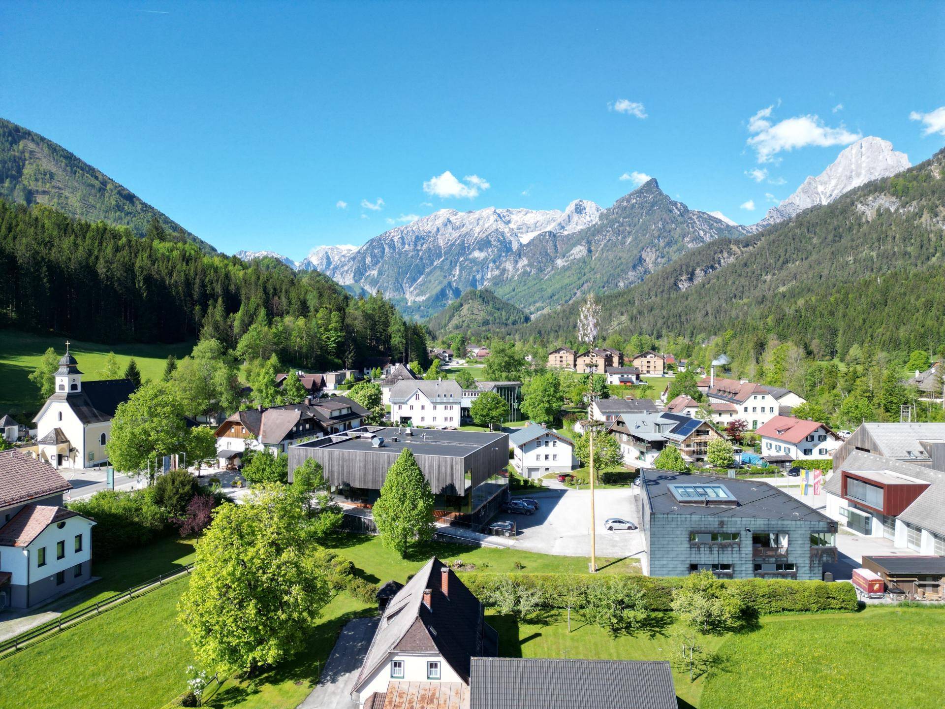 Panoramablick auf ein malerisches Dorf in den Alpen mit grünen Wiesen und Bergen.