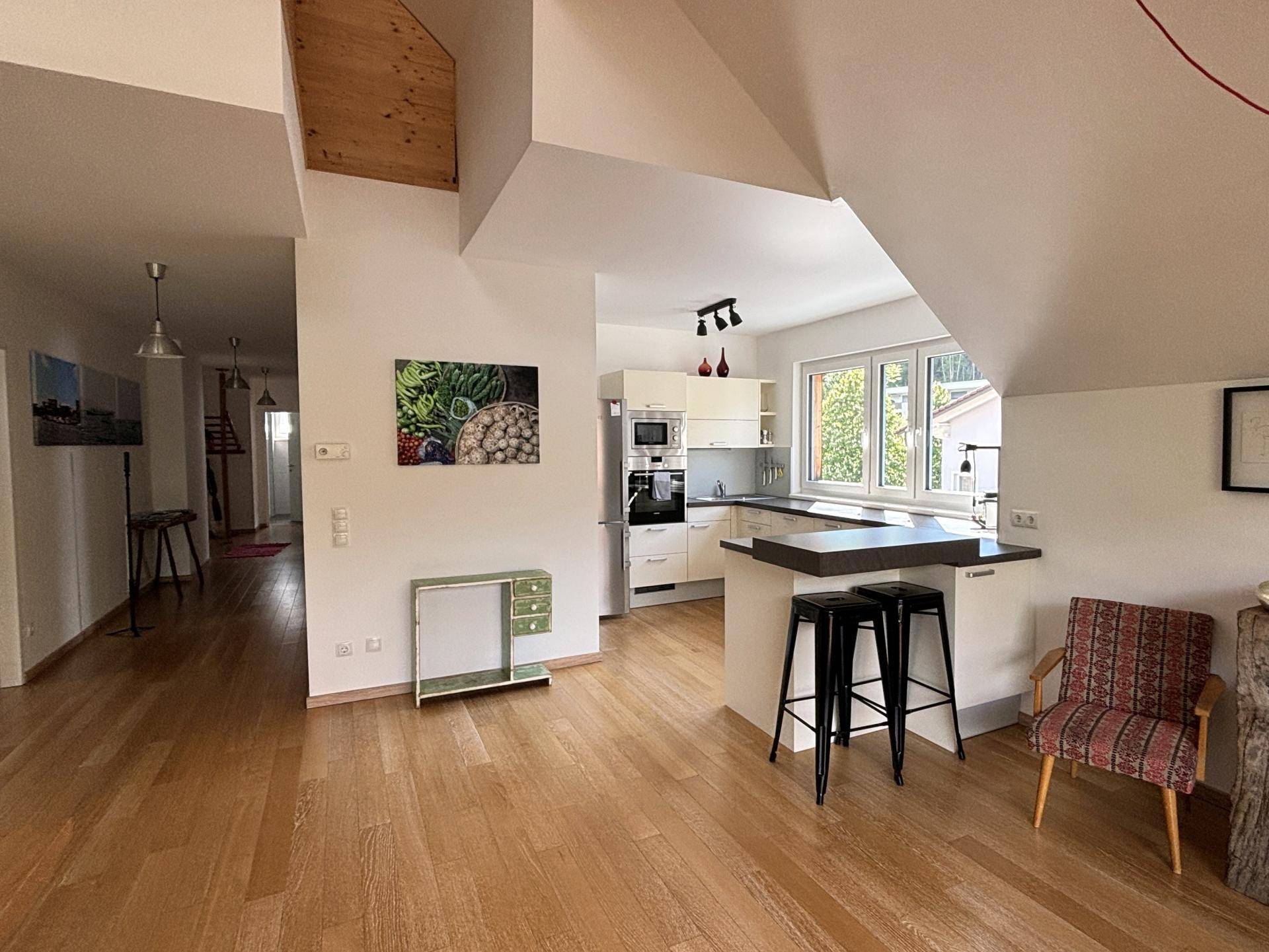 Moderne offene Küche mit Kücheninsel, Holzboden und Blick ins Grüne.