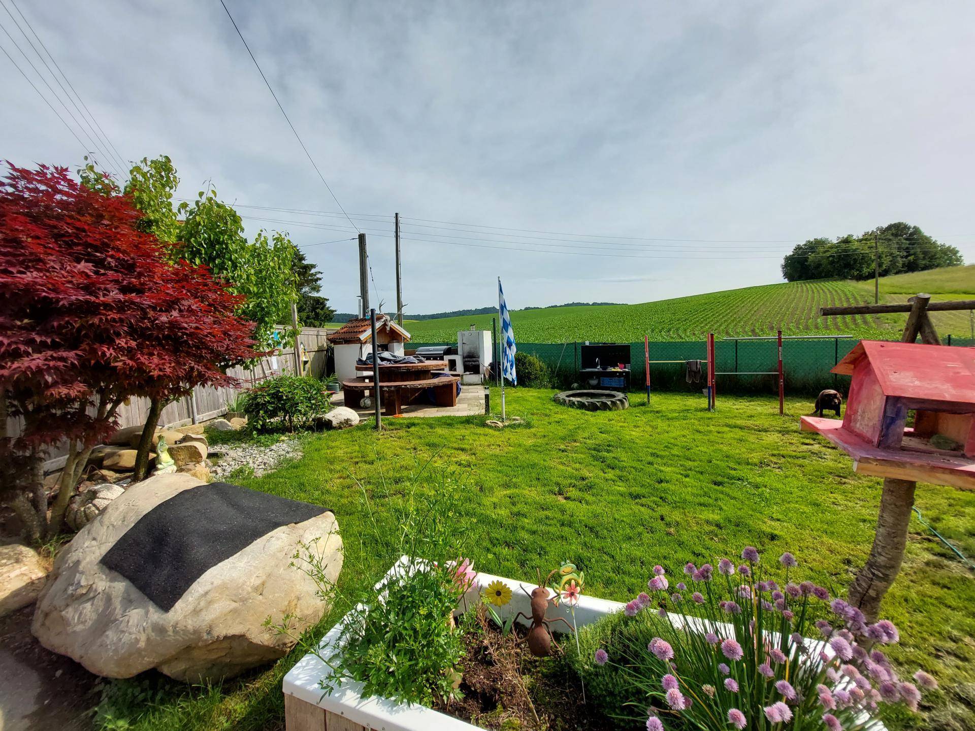 Gepflegter Garten mit Rasenfläche, Sitzbereich und weitem Blick auf die umliegende Landschaft.