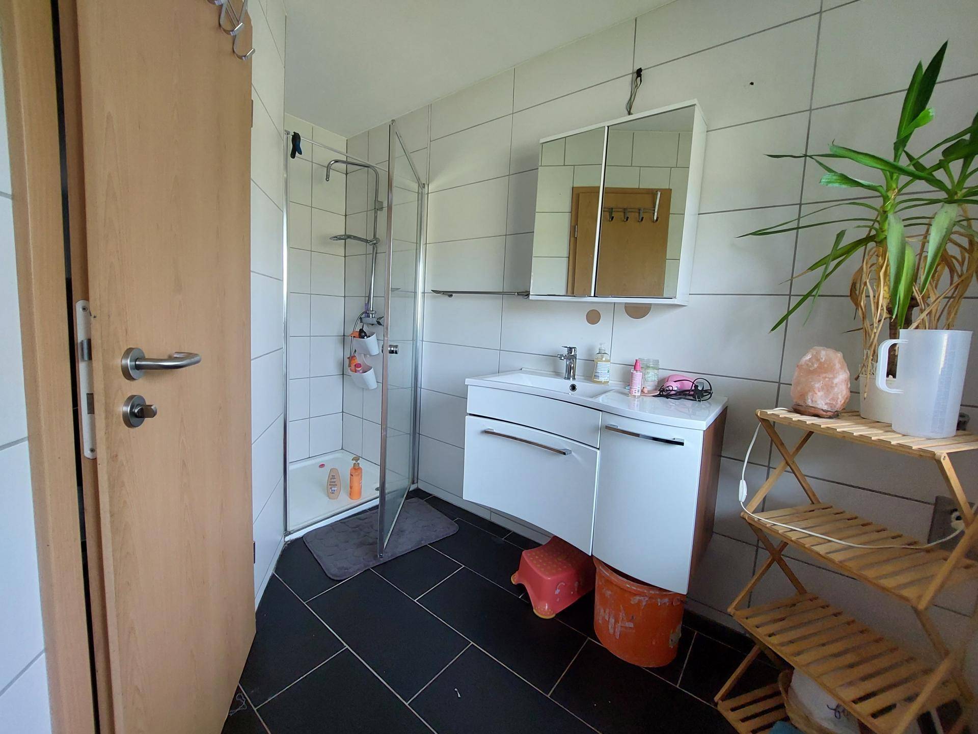 Helles Badezimmer mit weißen Wandfliesen, schwarzem Boden und moderner Duschkabine.