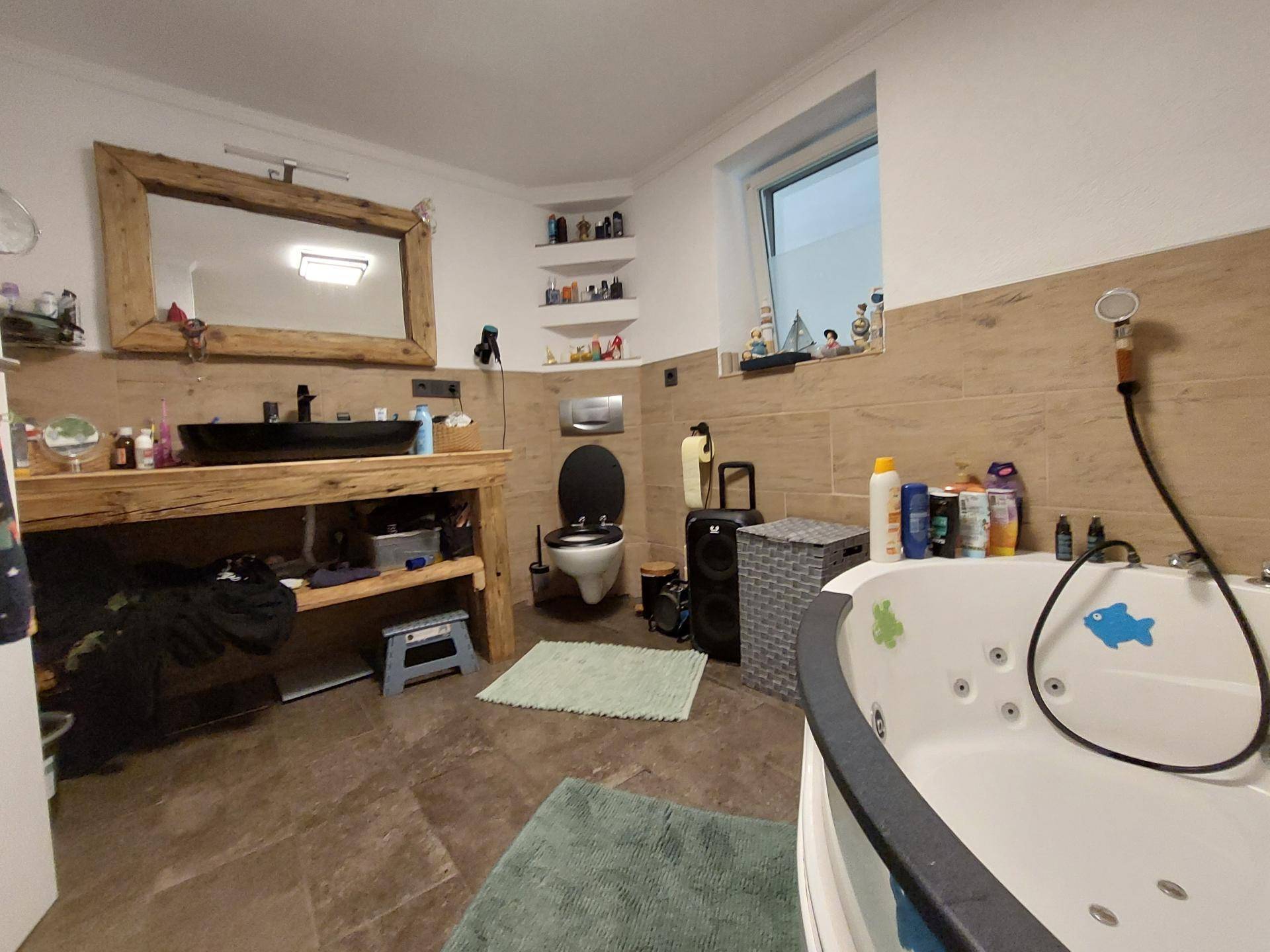 Geräumiges Badezimmer mit Eck-Whirlpool, Holzwaschtisch und Fenster für natürliches Licht.