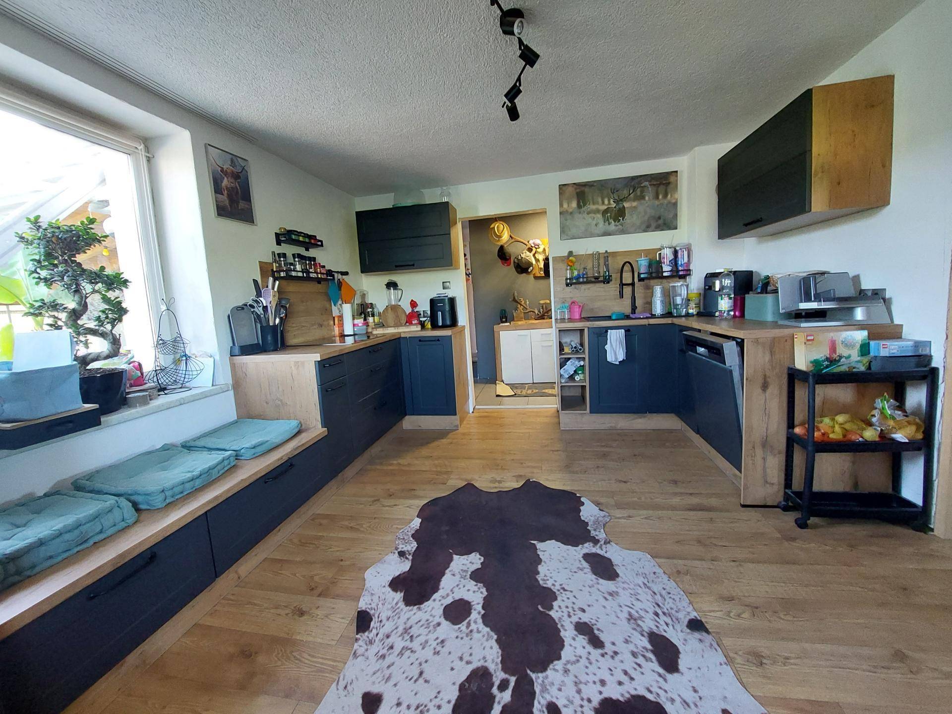 Moderne Küche mit dunklen Unterschränken, Holzarbeitsplatten und großem Fenster mit Sitzbank.