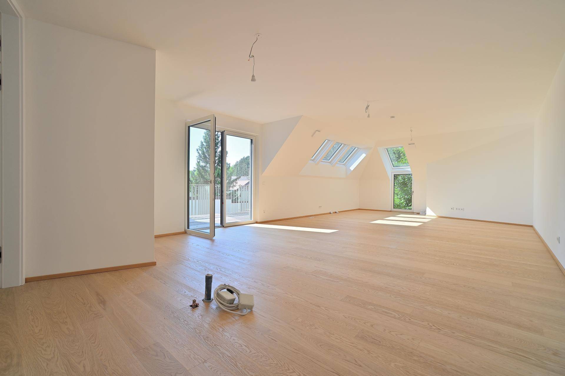 Heller Dachgeschoss-Wohnbereich mit Parkettboden, Dachfenstern und Zugang zu einem Balkon.