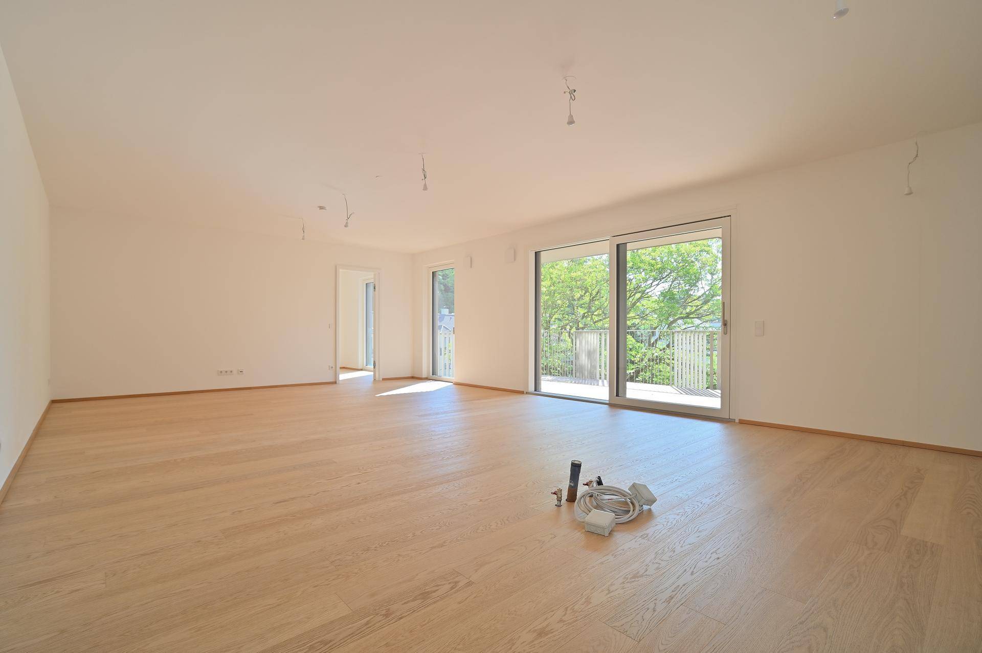 Geräumiger, heller Wohnbereich mit Parkettboden und großen Fenstern mit Zugang zum Balkon.