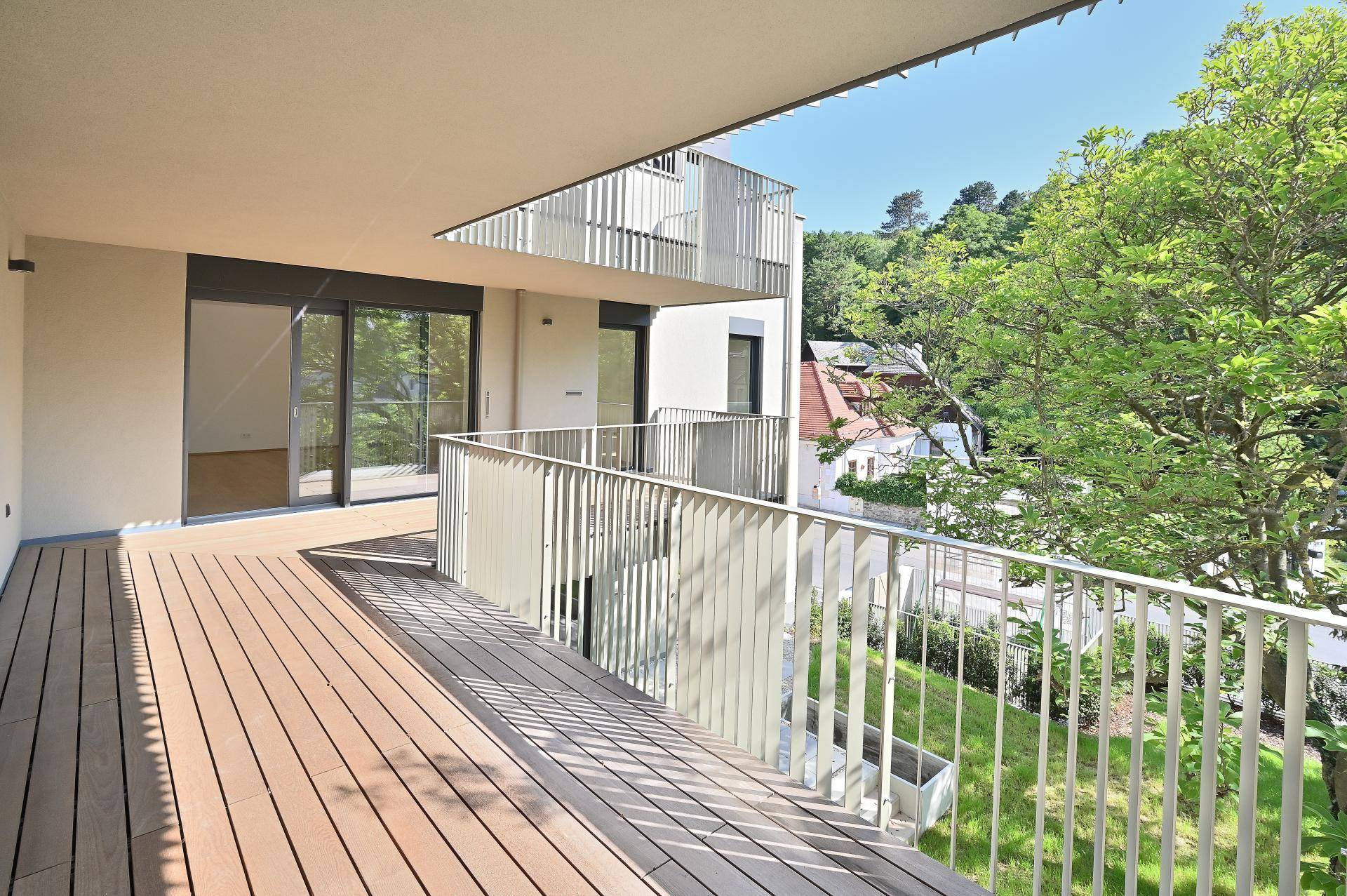 Geräumiger Balkon mit Holzboden und Metallgeländer, bietet einen weiten Blick ins Grüne.