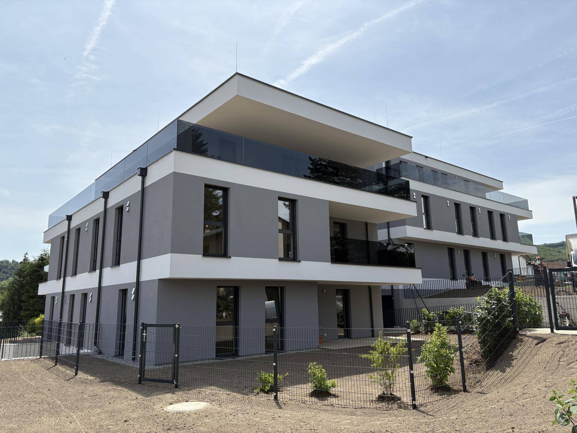 Modernes Mehrfamilienhaus mit klaren Linien und großen Glasbalkonen unter blauem Himmel.