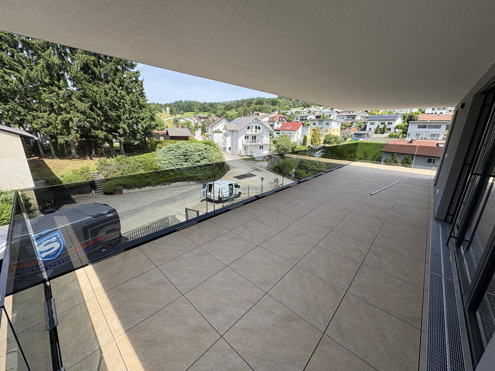 Geräumige, geflieste Terrasse mit Glasgeländer und Blick auf die umliegende Wohngegend.