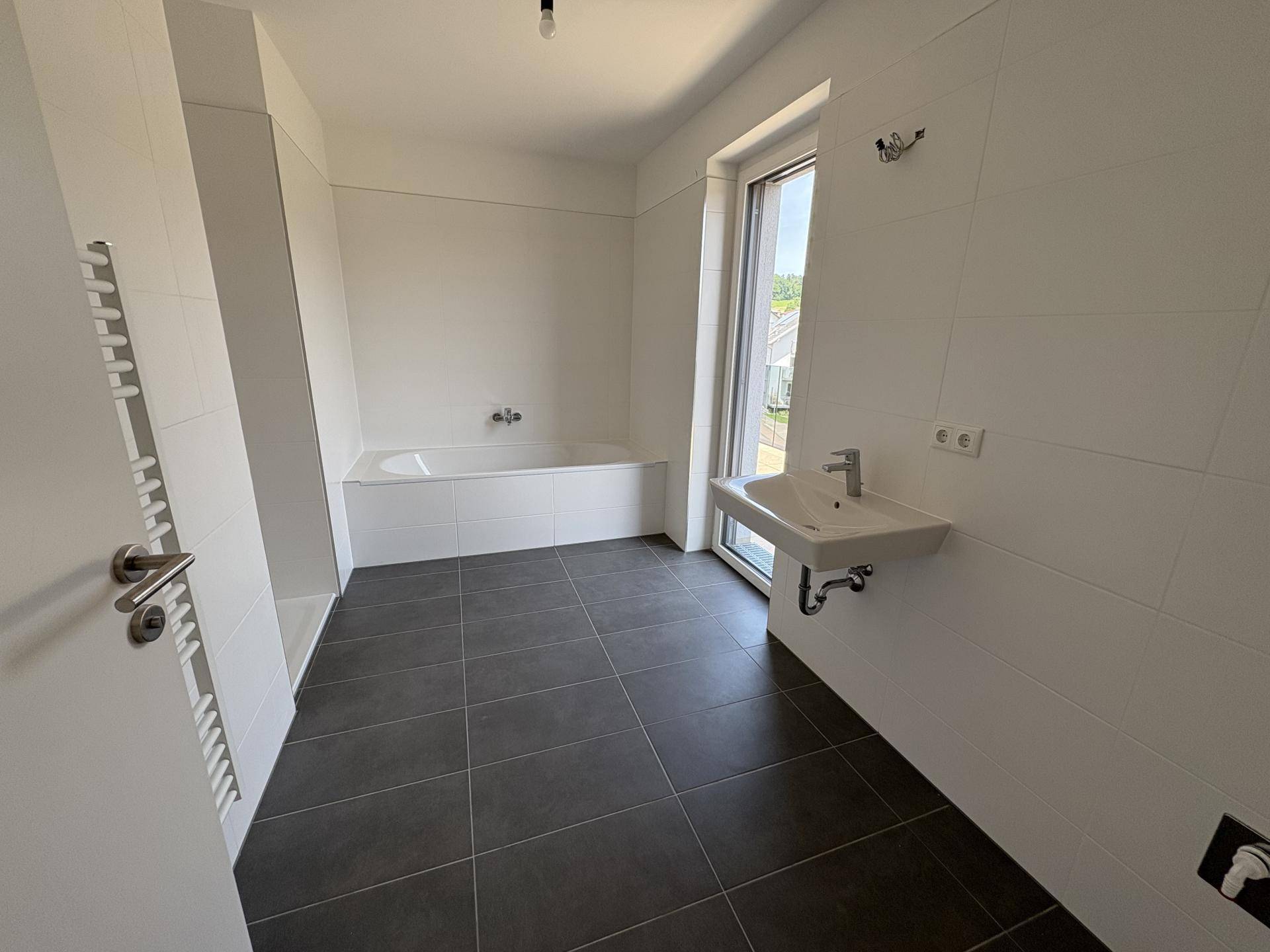 Modernes Badezimmer mit Badewanne, Einzelwaschbecken und Fenster für Tageslicht.