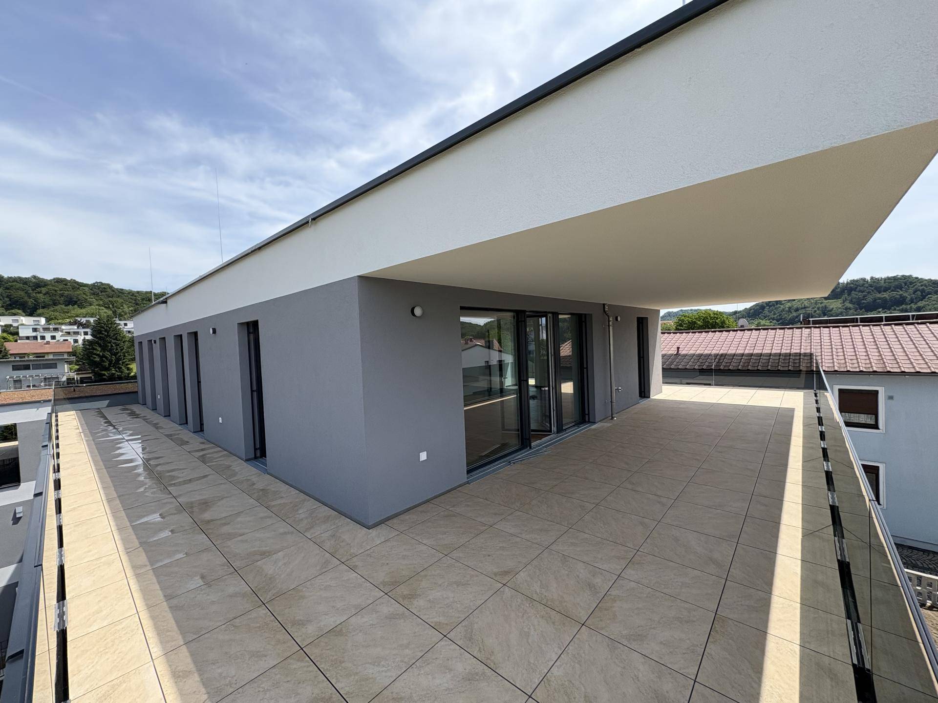 Moderne Architektur mit großer, gefliester Terrasse und klaren Linien unter blauem Himmel.