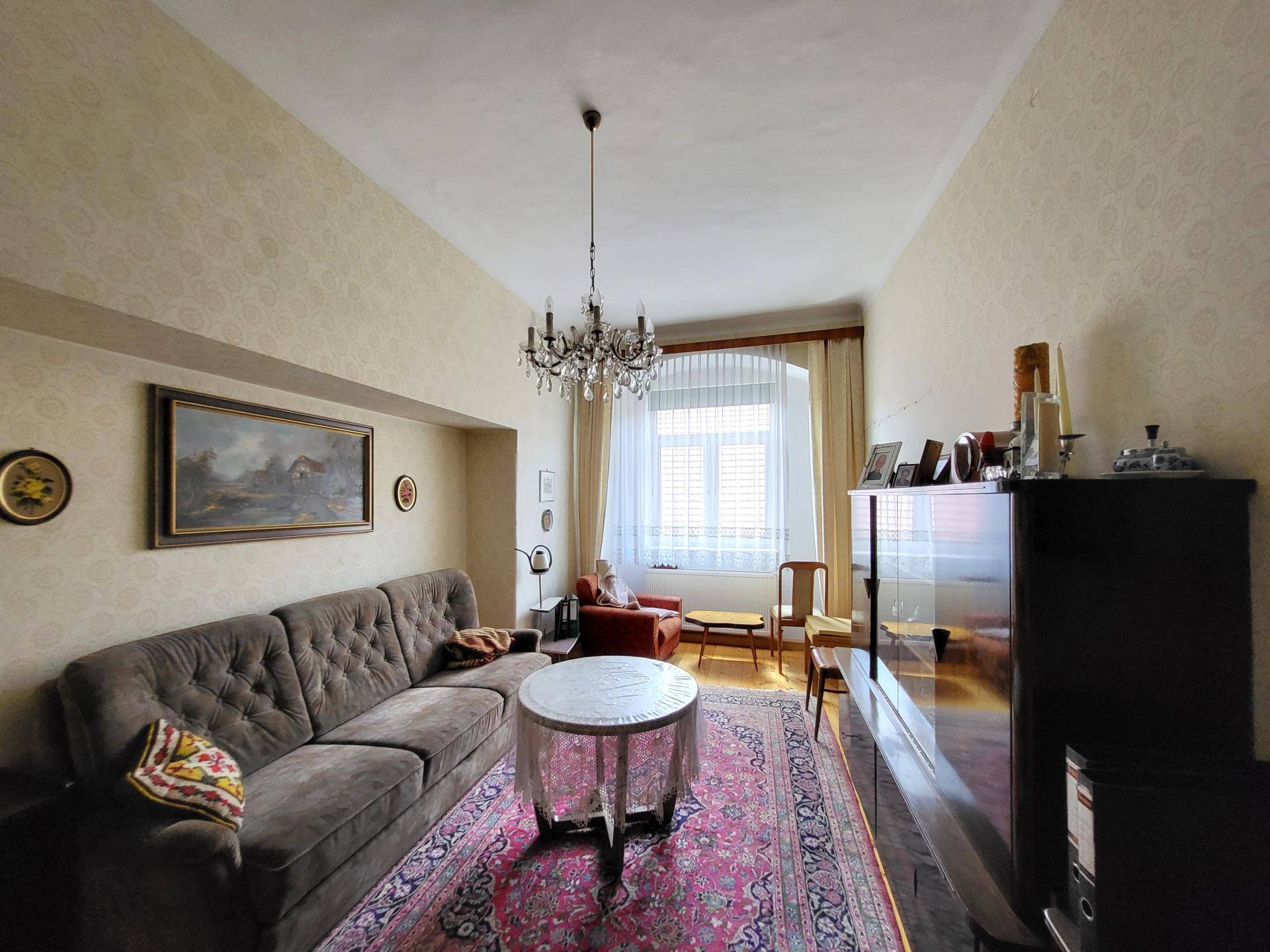 Gemütliches Wohnzimmer mit traditionellen Möbeln, einem Kronleuchter und gemusterter Tapete.