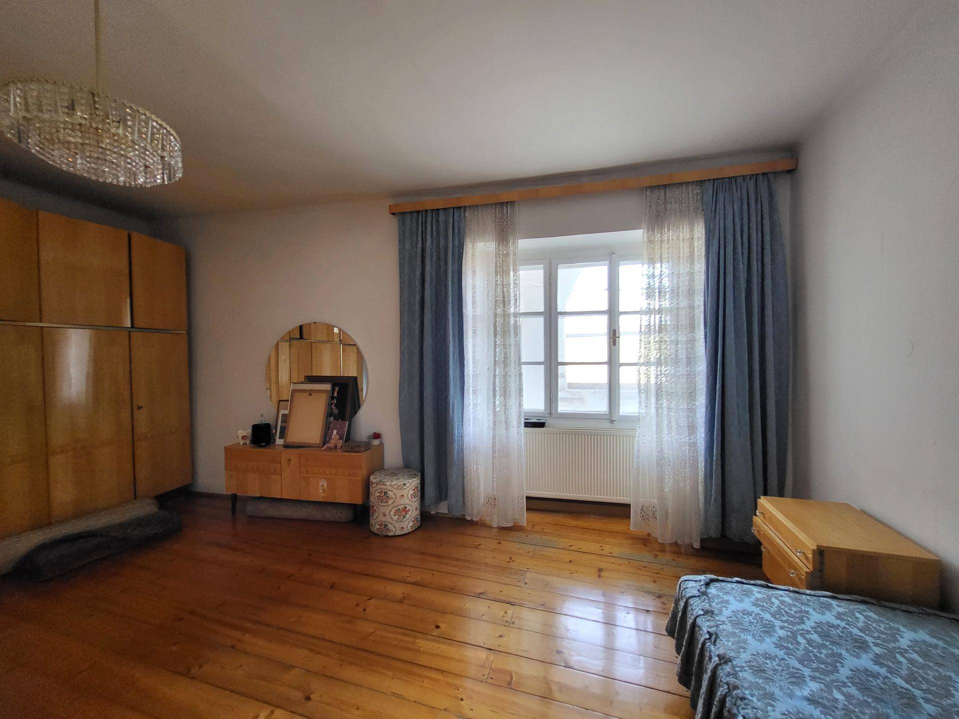 Schlafzimmer mit breiten Holzfußbodendielen, einem großen Fenster und einem Kleiderschrank aus Holz.