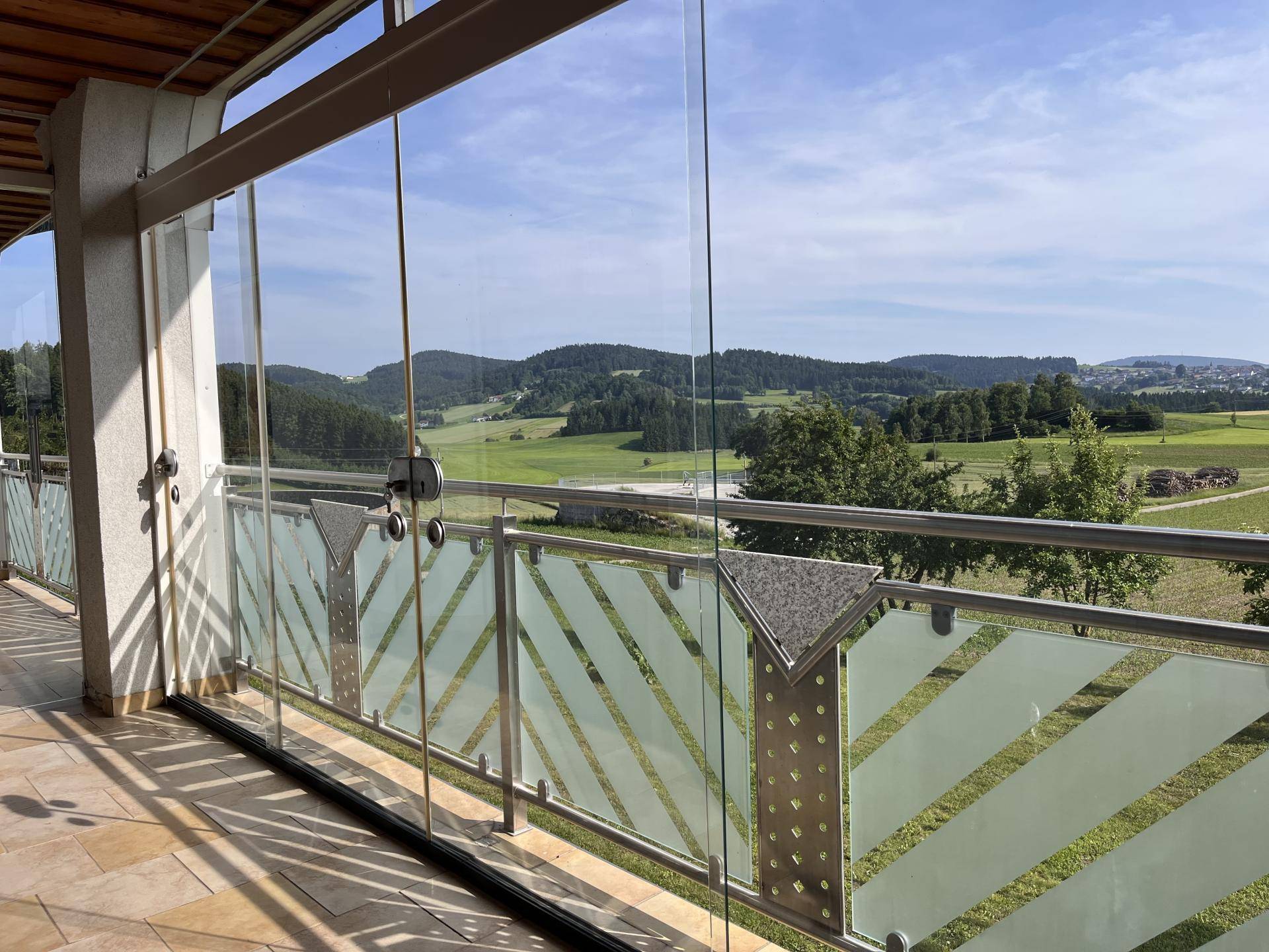 Heller, verglaster Balkon mit Fliesenboden und Panoramablick auf die hügelige Landschaft.