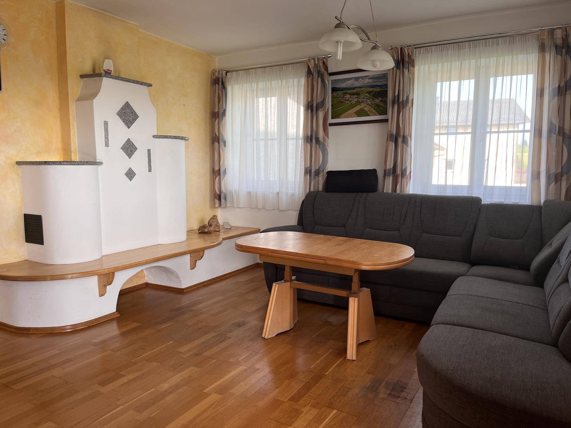 Gemütliches Wohnzimmer mit Kachelofen, Holzboden und bequemer Eckcouch.