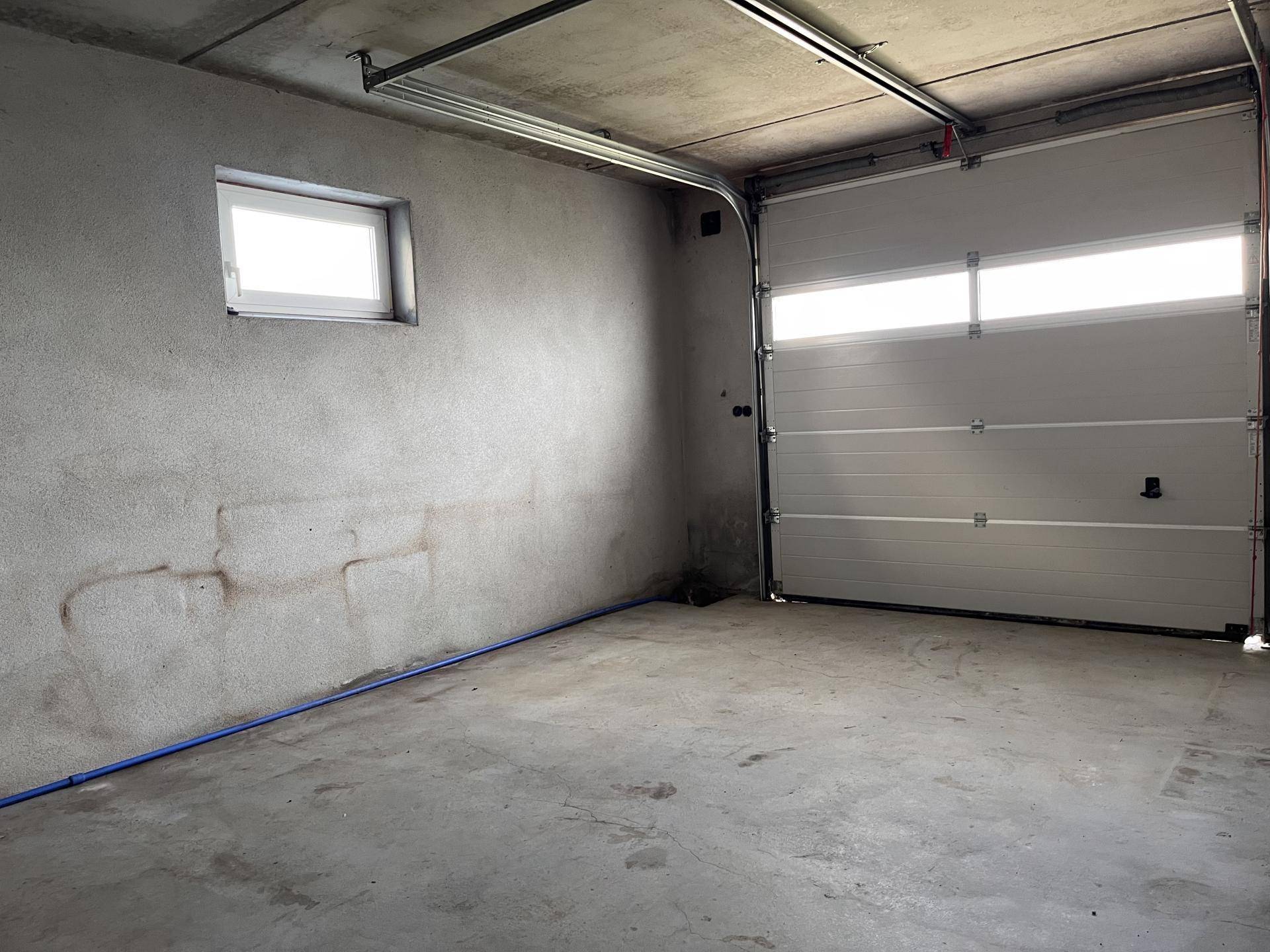 Leere Garage mit Betonboden, Sektionaltor und kleinem Fenster.