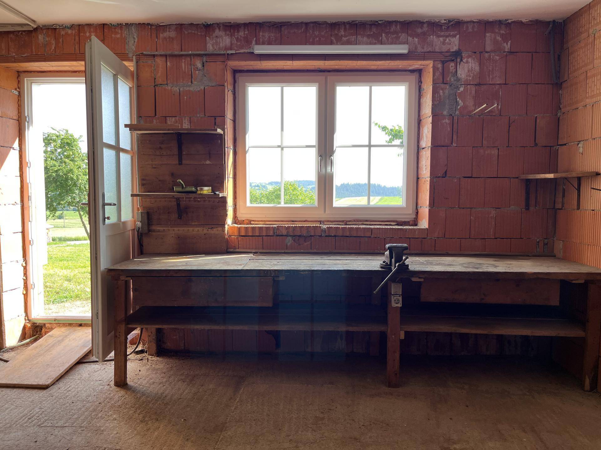 Werkstattraum mit Werkbank, Fenster und Blick ins Grüne, noch im Rohbau.