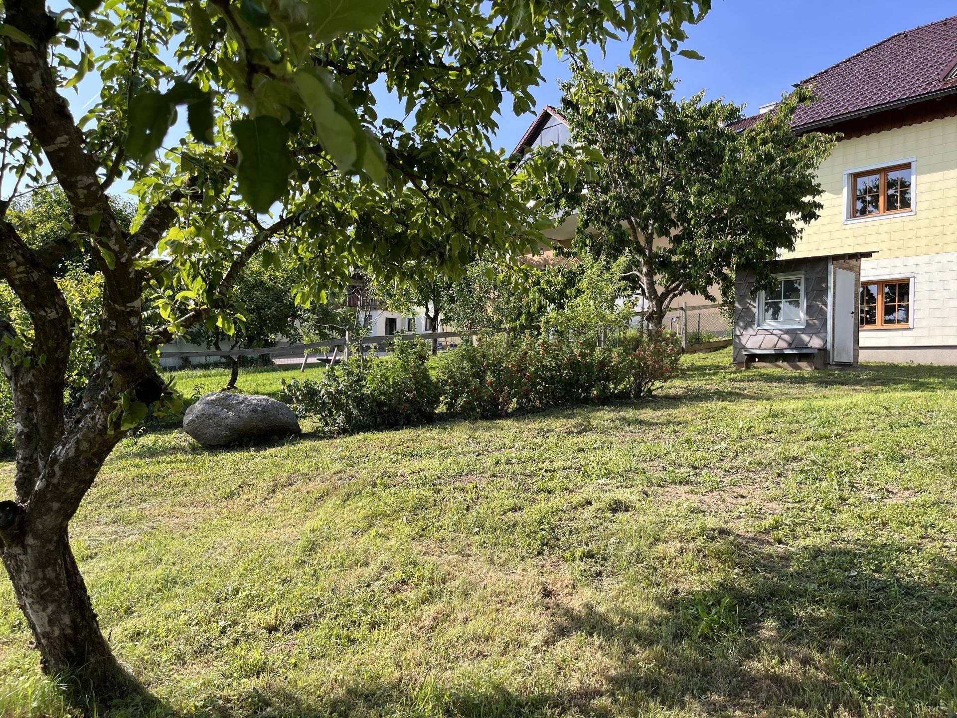Gepflegter Garten mit Rasenfläche, Sträuchern und einem großen Stein im Vordergrund.