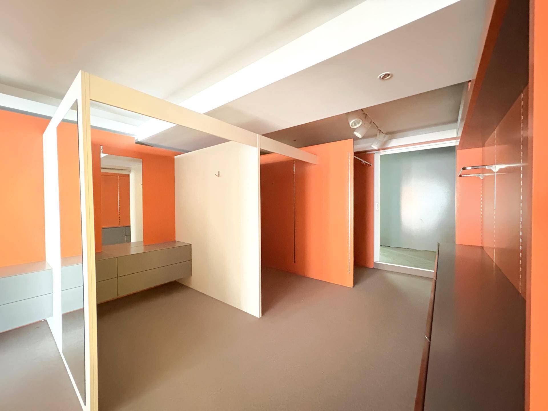 Moderner Verkaufsraum mit orangefarbenen Akzenten, grauen Böden und Umkleidekabinen.