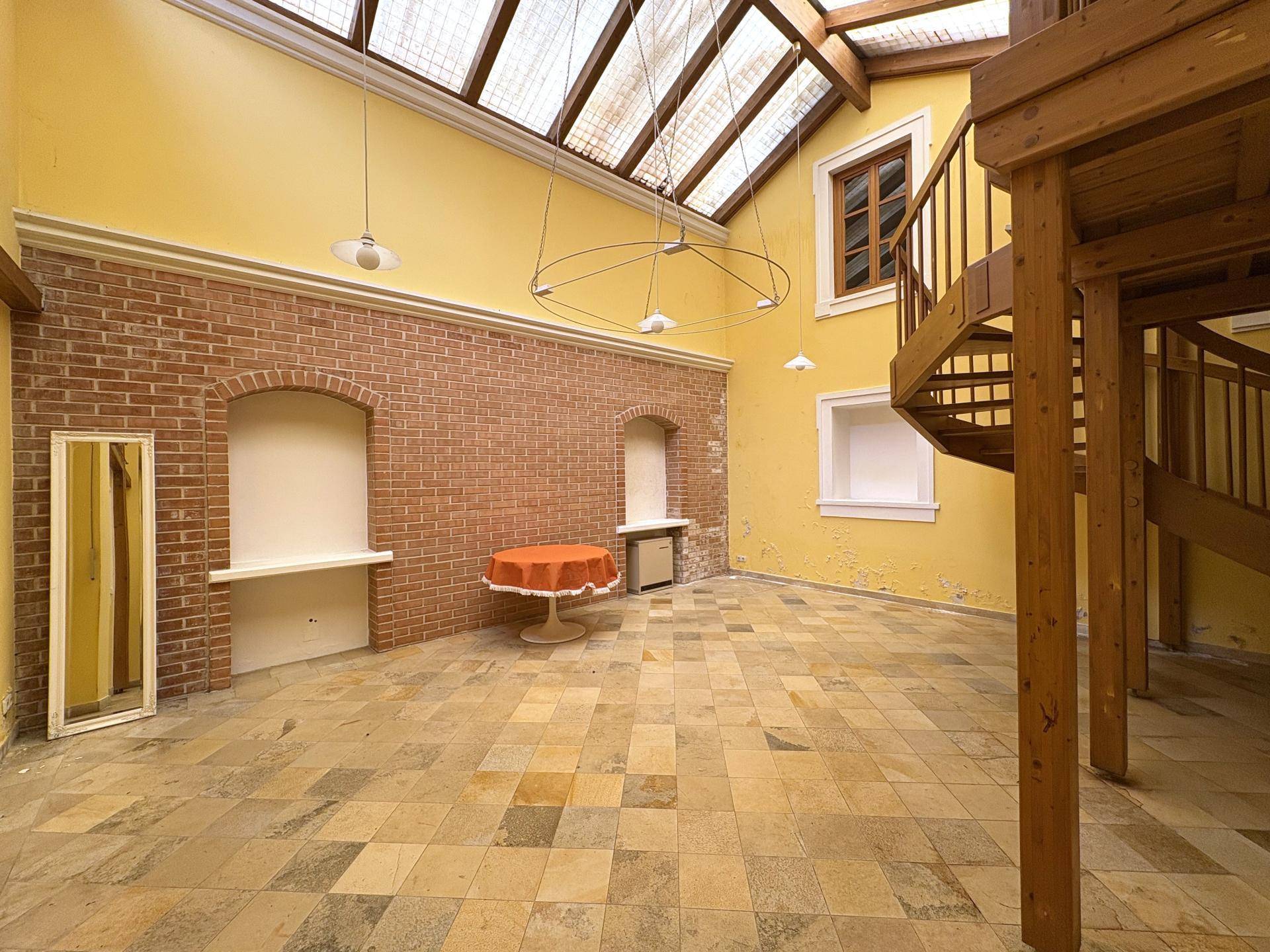 Geräumiges Atrium mit hohen gelben Wänden, Holzbalken und einer beeindruckenden Wendeltreppe.