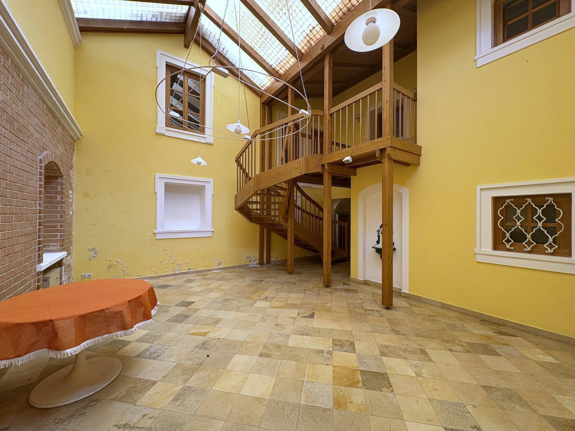 Beeindruckendes Atrium mit einer eleganten Holzwendeltreppe, hohen Decken und viel Tageslicht.