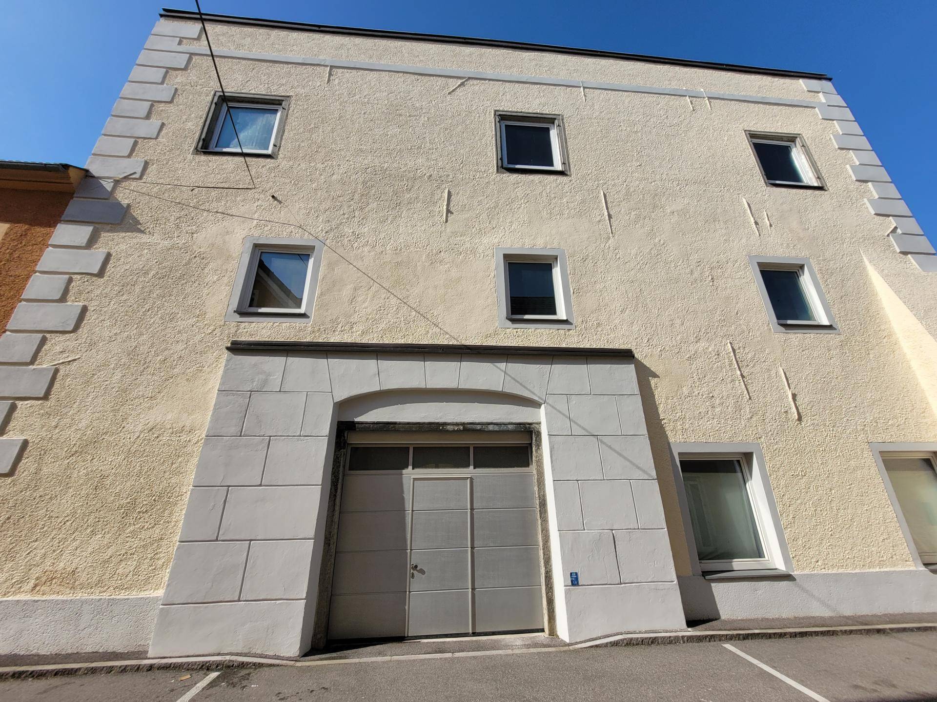 Fassade eines Gebäudes mit mehreren Fenstern und einem großen Garagentor im Erdgeschoss.