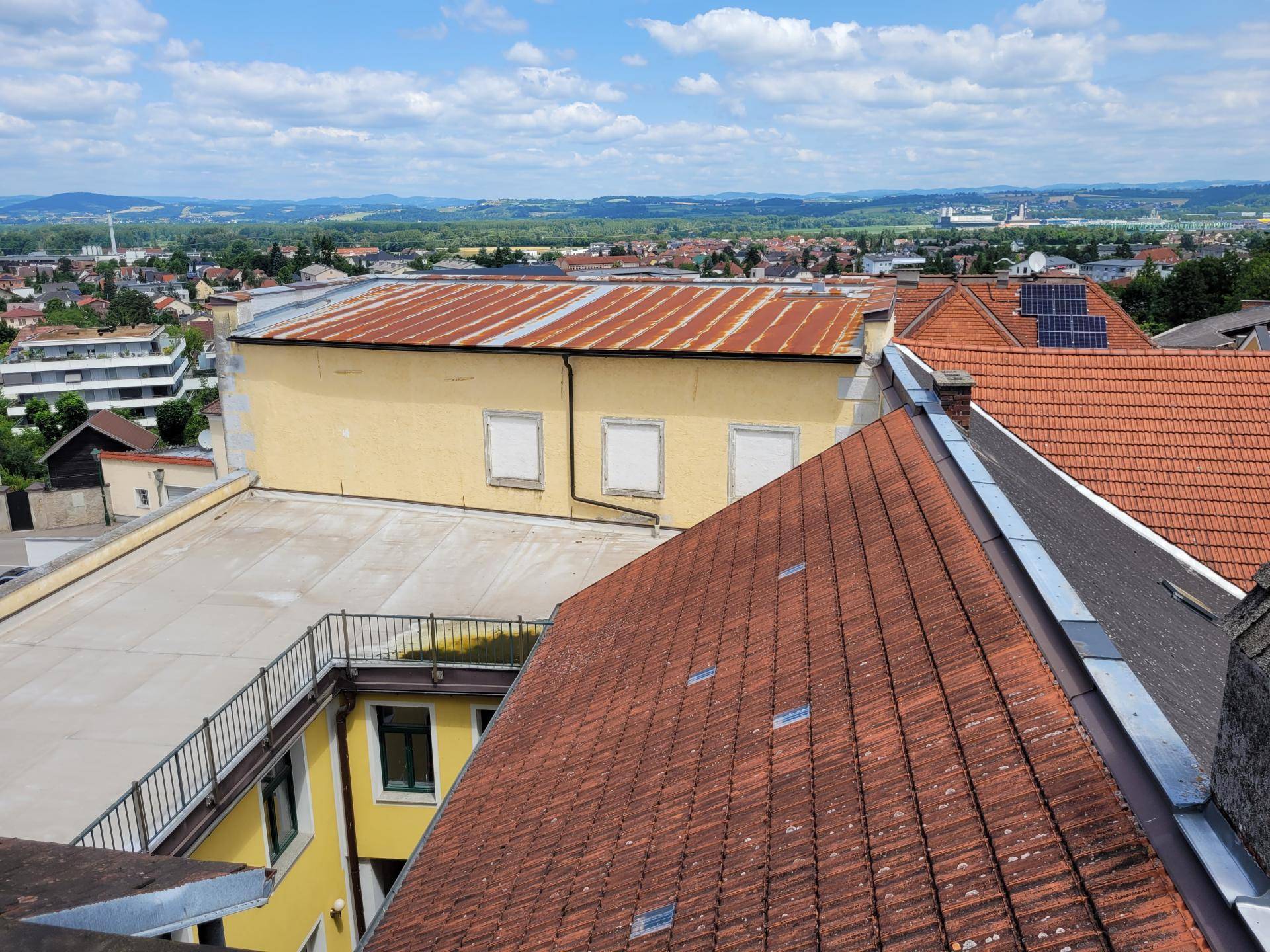 Panoramablick über Dächer und die weite Landschaft mit Bergen und einem blauen Himmel.