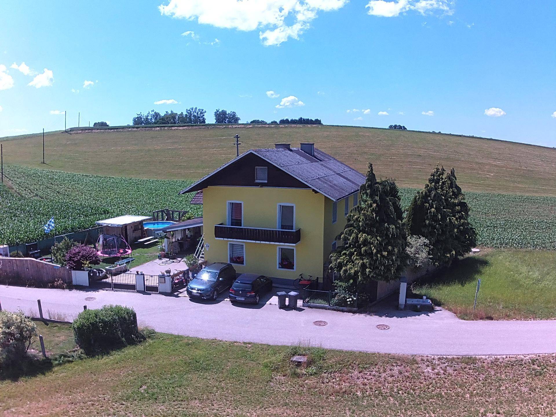 Gelbes Einfamilienhaus mit Satteldach, umgeben von grünen Feldern unter blauem Himmel.