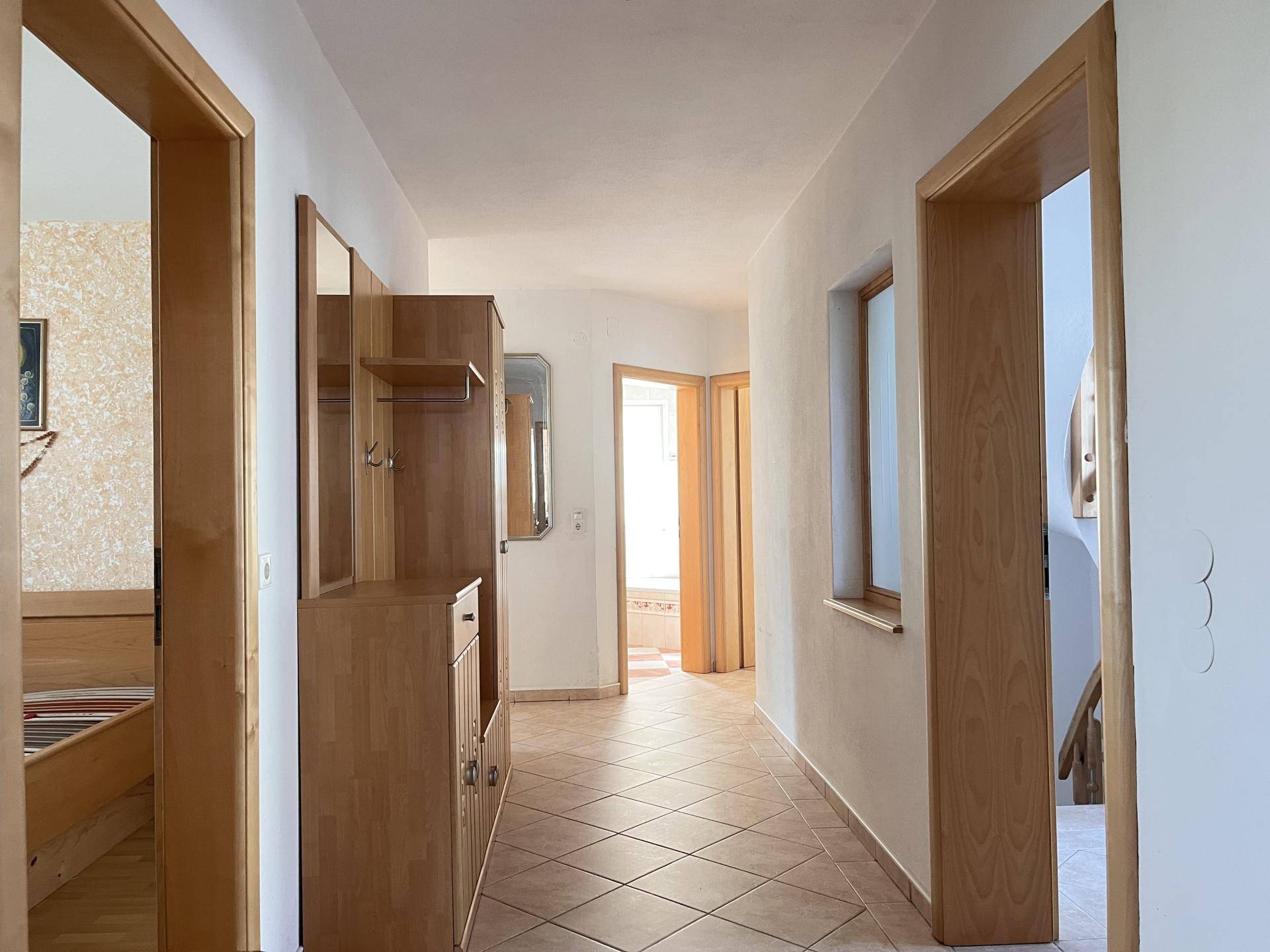Heller Flur mit Fliesenboden und Garderobe, der zu verschiedenen Räumen führt.