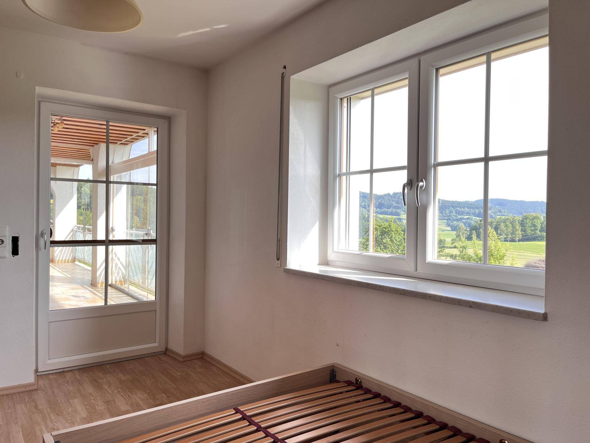 Helles Schlafzimmer mit Zugang zum Balkon und weitem Blick über die Landschaft.