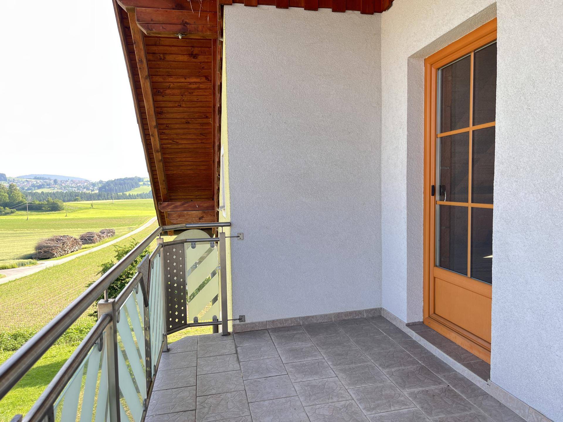 Kleiner Balkon mit Fliesenboden und Geländer, bietet einen weiten Blick ins Grüne.