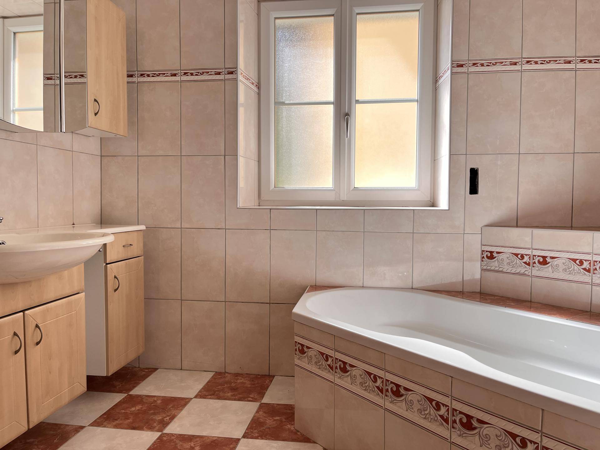 Badezimmer mit Eckbadewanne, Fliesenboden und Fenster für Tageslicht.