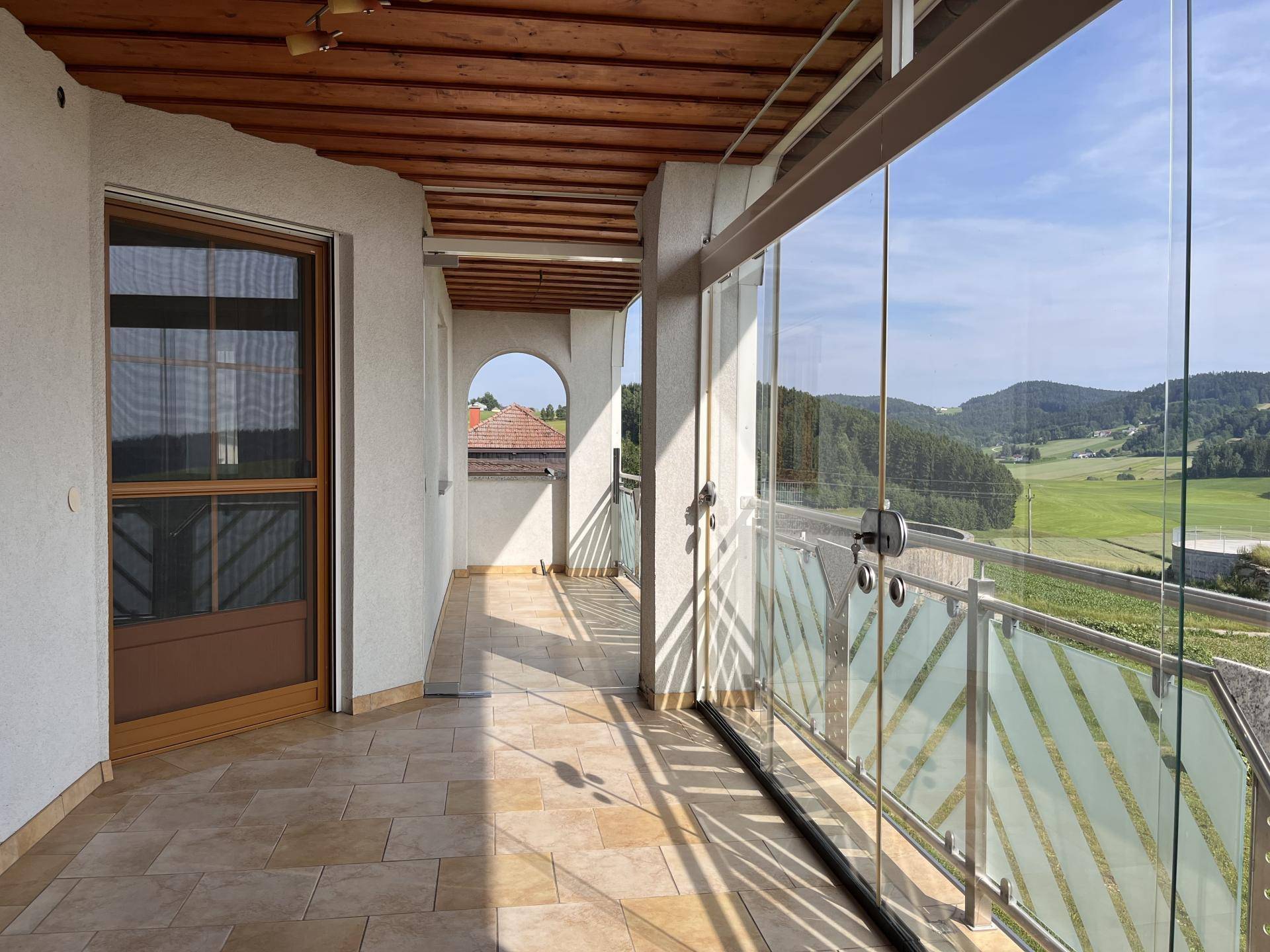 Verglaster Balkon mit Fliesenboden und weitem Blick über die grüne Landschaft.