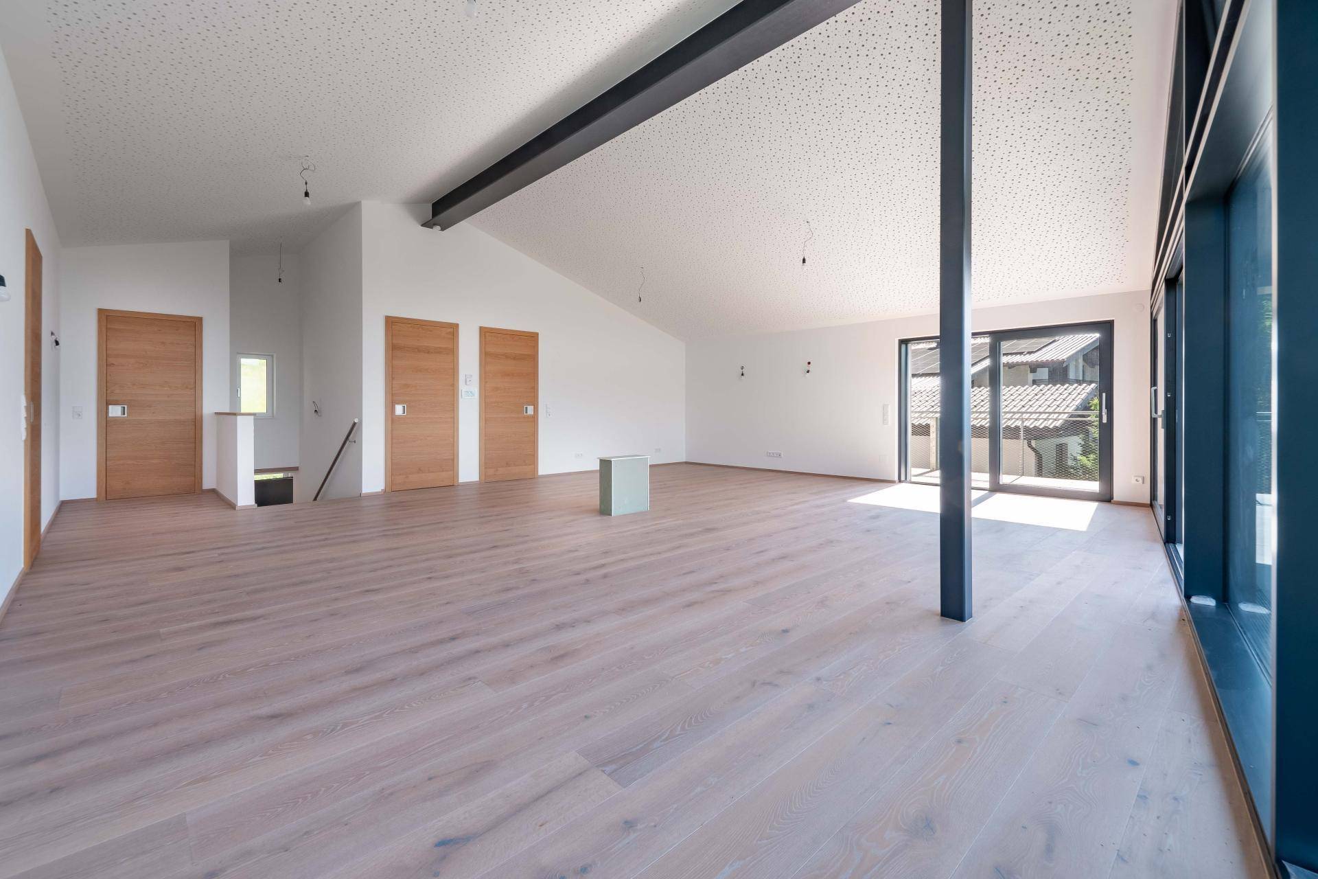 Heller, offener Wohnbereich im Dachgeschoss mit Holzboden, großen Fenstern und Zugang zum Außenbereich.