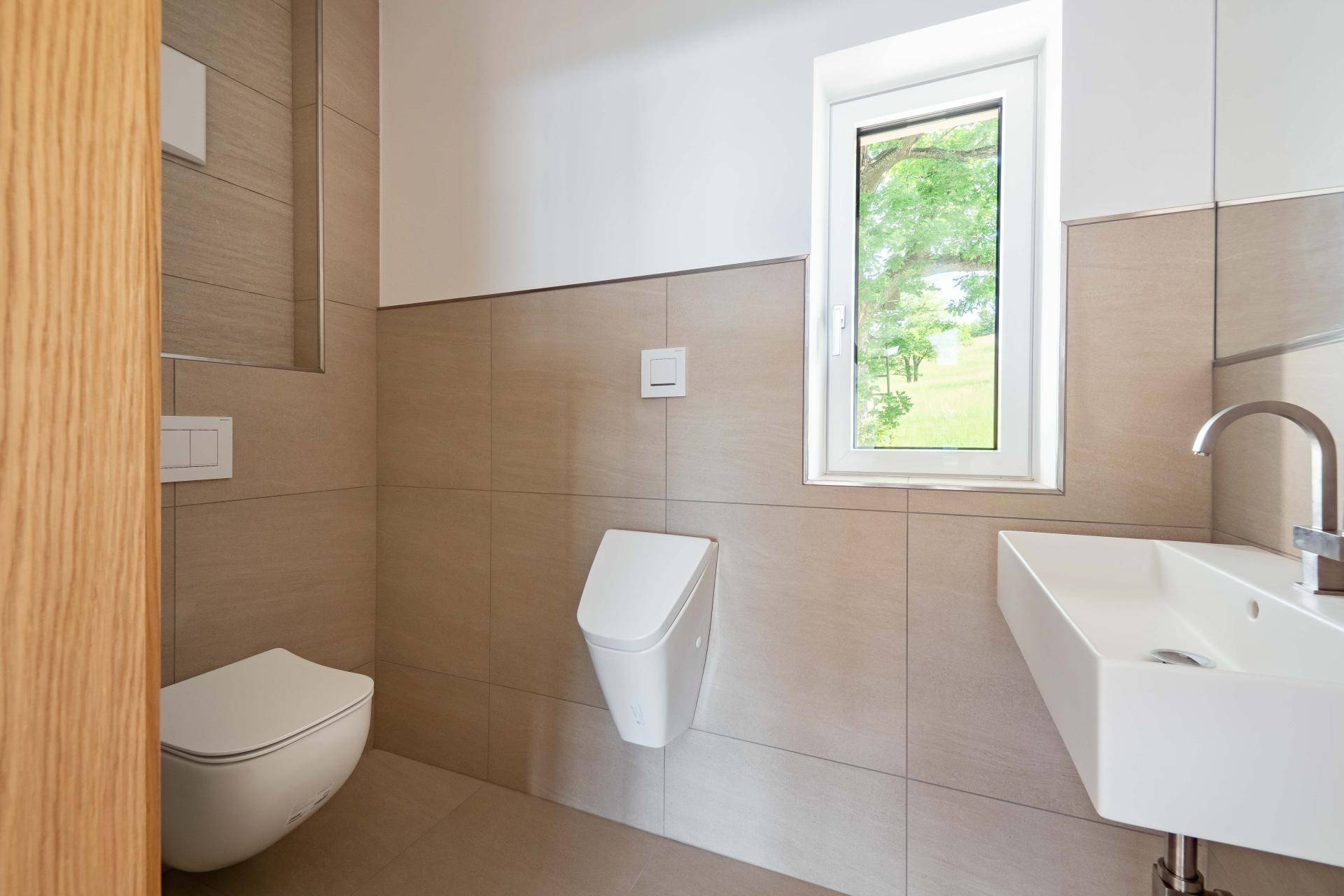Modernes Gäste-WC mit Wand-WC, Urinal, Waschbecken und Fenster, hell gefliest.