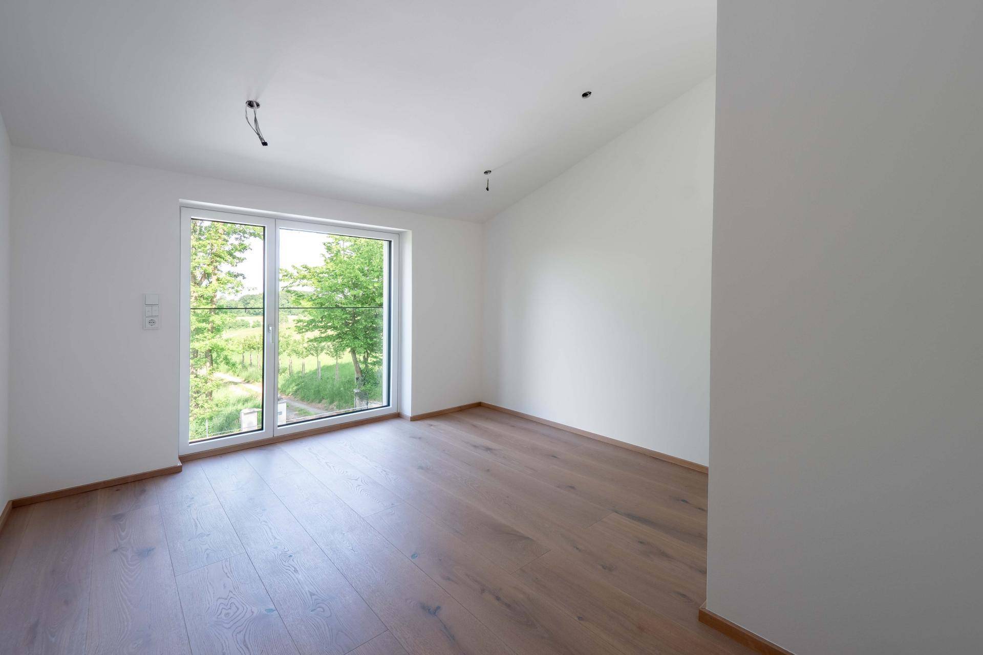 Helles Zimmer mit Holzboden und großem Fenster, das einen schönen Blick ins Grüne bietet.