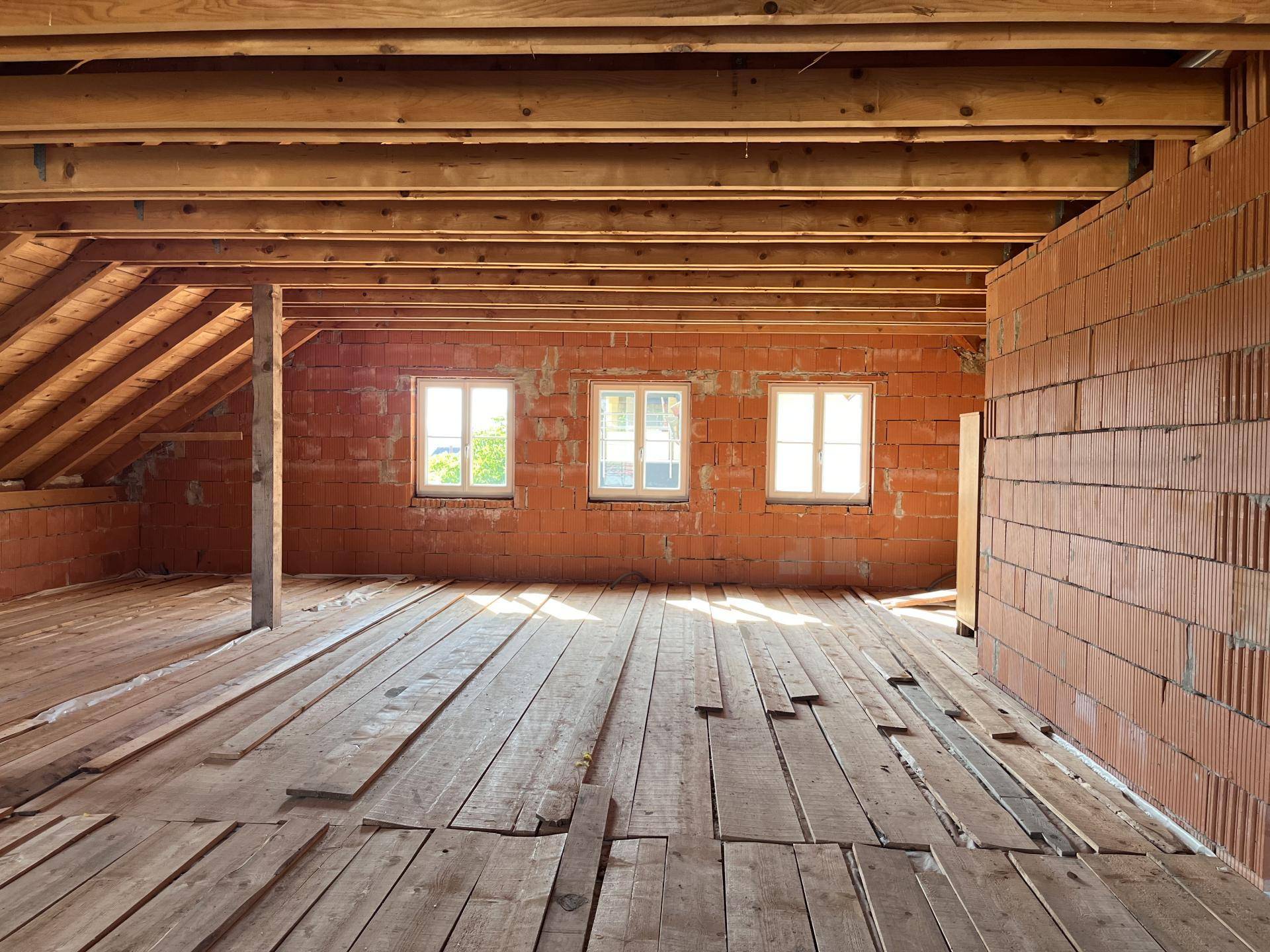 Großer Dachbodenraum mit sichtbaren Holzbalken und Fenstern, noch im Rohbau.