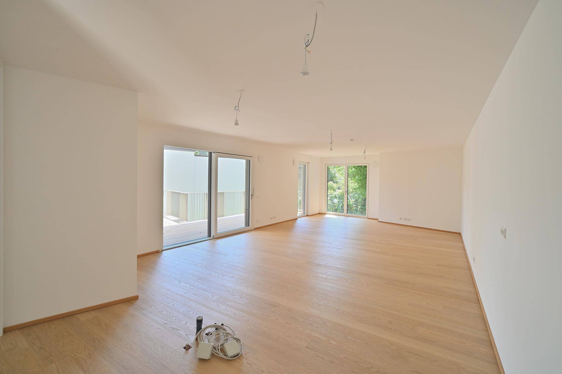 Heller, leerer Wohnbereich mit Eichenparkettboden und großen Schiebetüren zu Balkon und Garten.