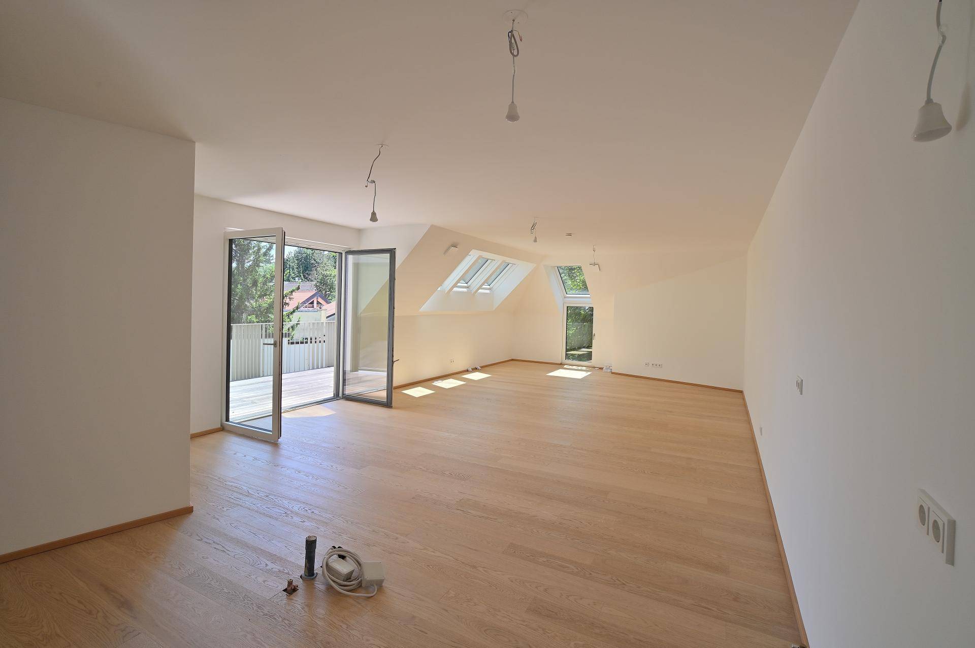 Geräumiger Dachgeschoss-Wohnbereich mit Parkettboden, vielen Fenstern und Zugang zum Balkon.