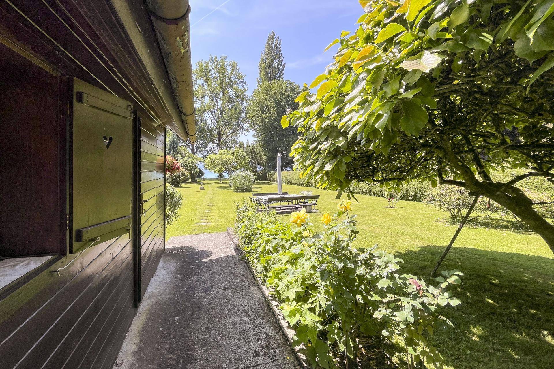 Blick aus einem Gebäude in den grünen Garten mit Rasenfläche und See im Hintergrund.