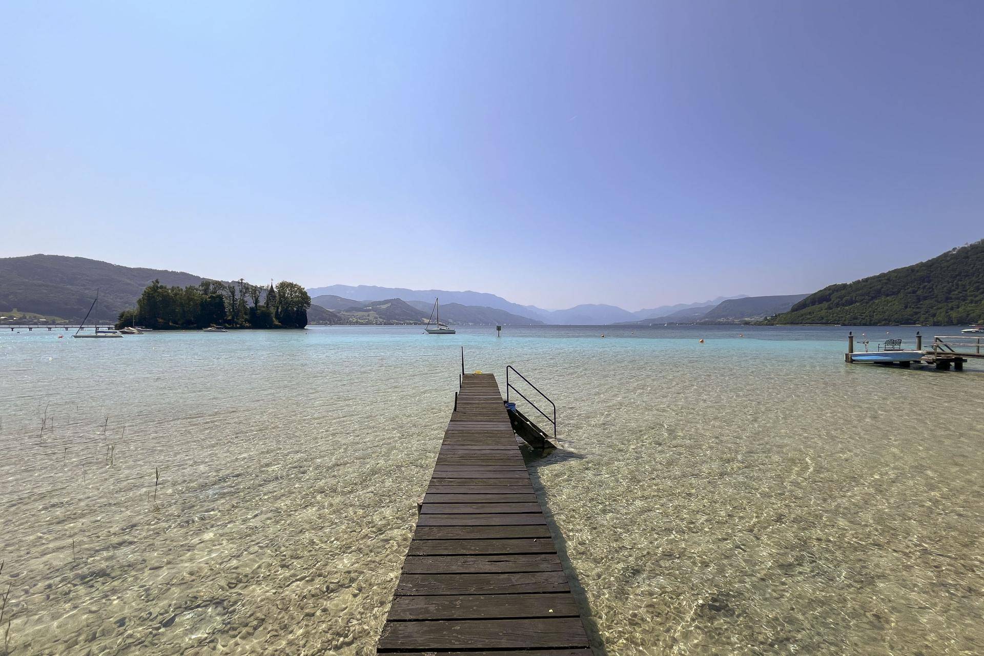 Langer Holzsteg ragt in das kristallklare Wasser eines Sees mit umliegenden Bergen.