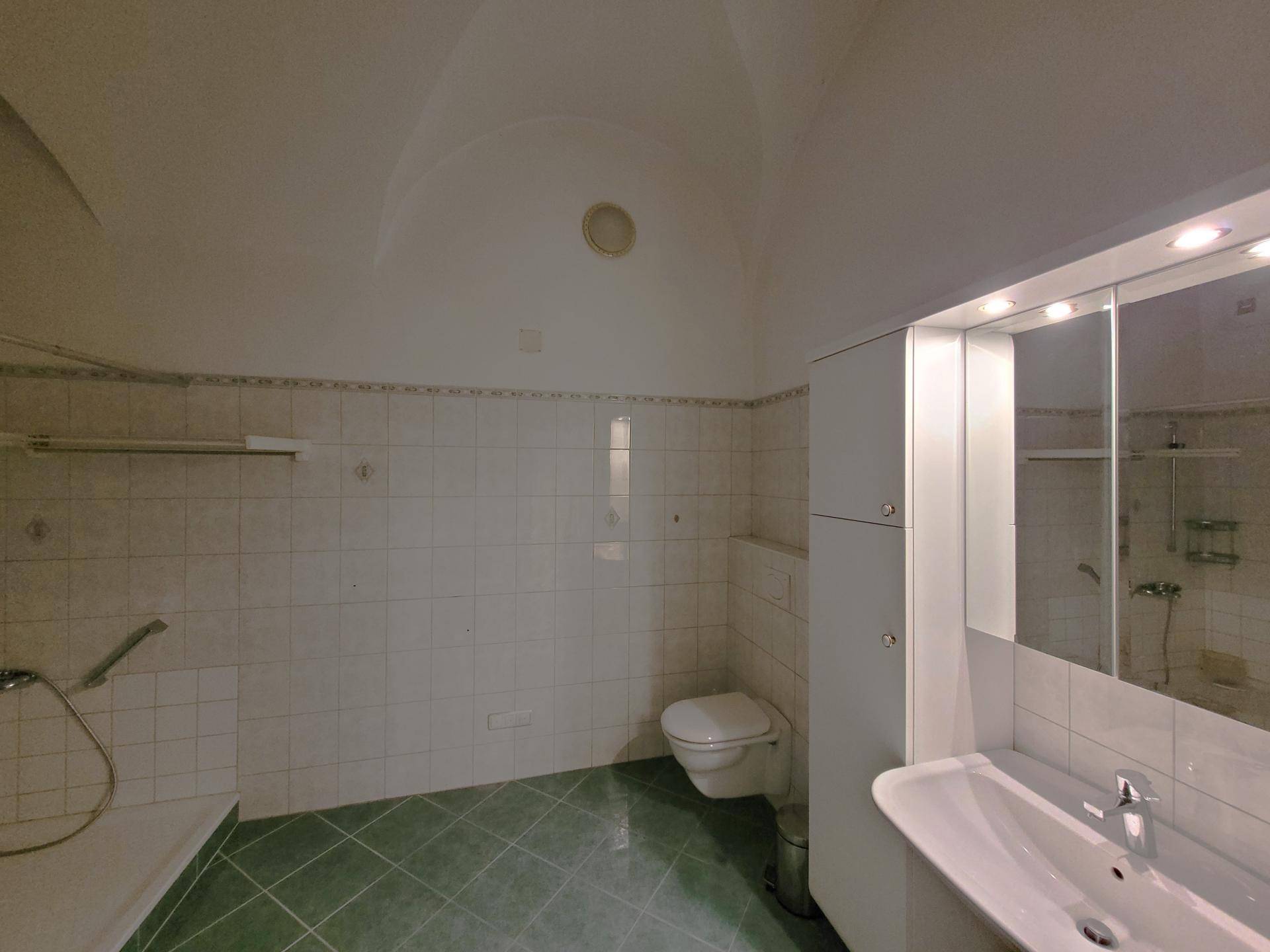Badezimmer mit grünen Bodenfliesen, weißen Wandfliesen, WC und Waschtisch mit Spiegelschrank.