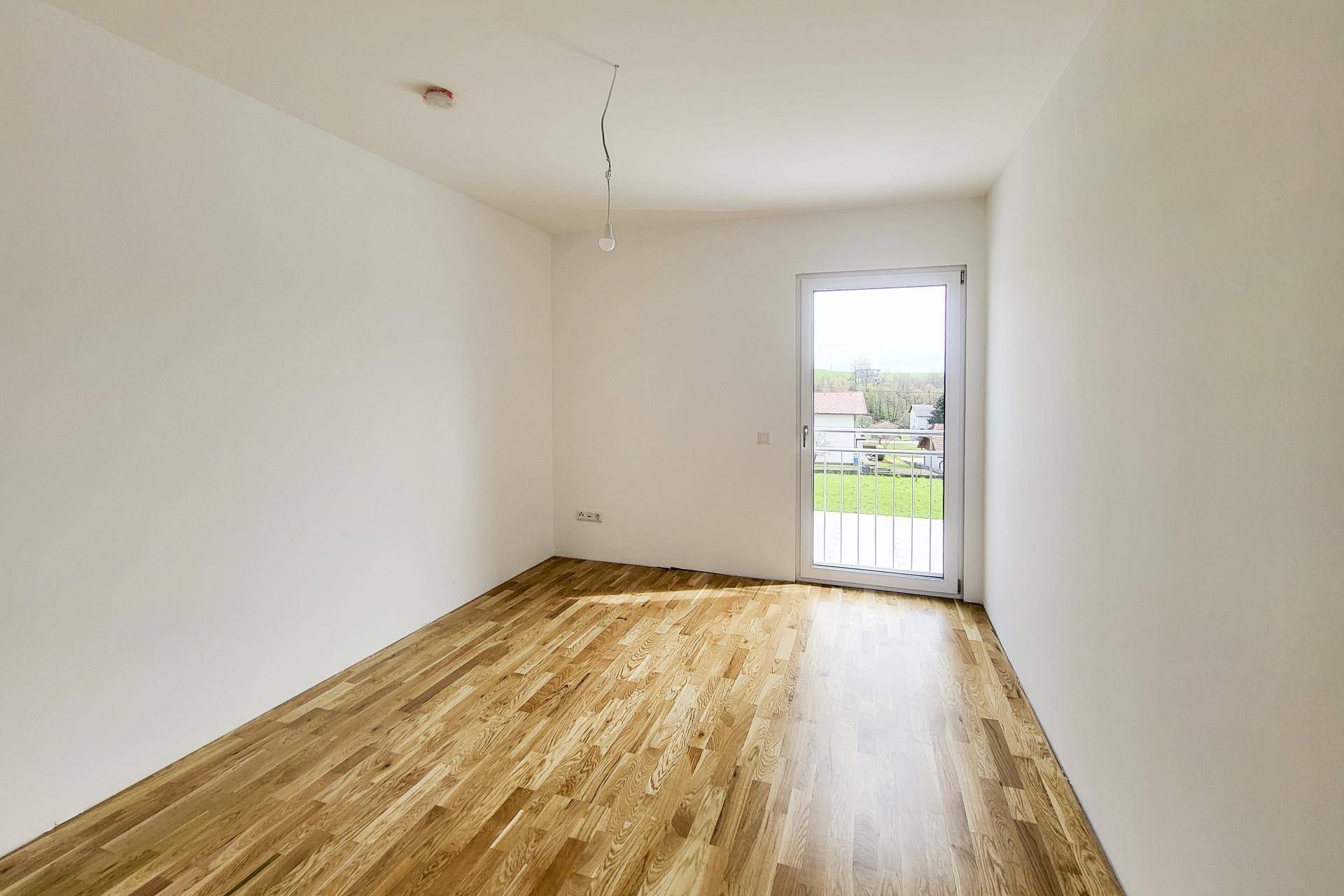 Lichtdurchfluteter Raum mit glänzendem Holzboden und Zugang zu einem kleinen Balkon.