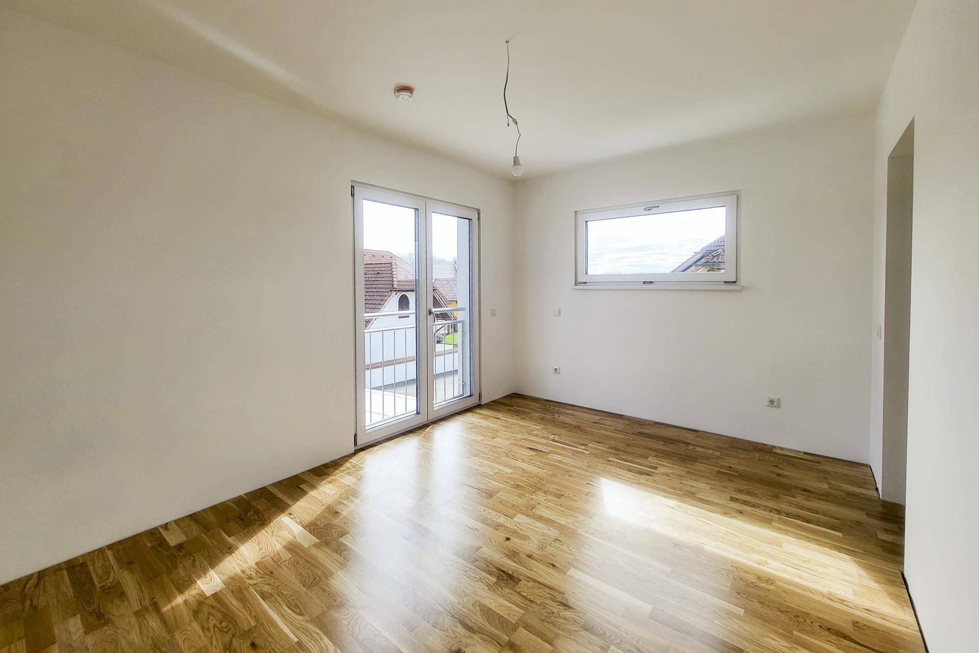 Helles Zimmer mit Holzboden und Zugang zu einem französischen Balkon, bietet viel Tageslicht.