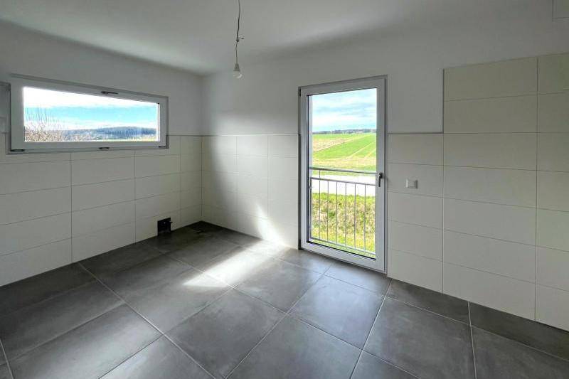 Heller Raum mit Fliesenboden und gefliesten Wänden, vorbereitet für eine Küche mit Balkonzugang.